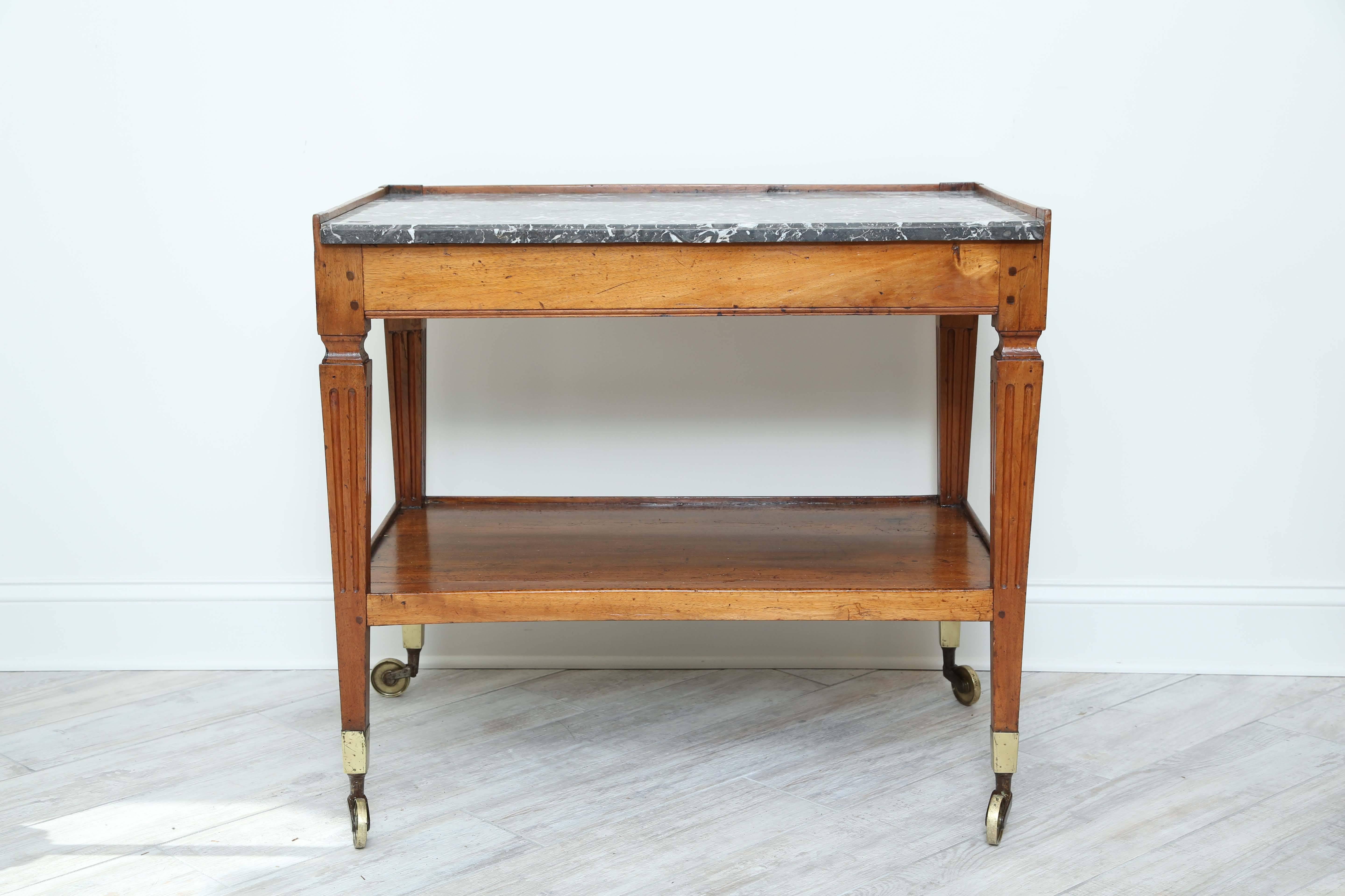 Antique two-tiered cart/work table with gray marble top and brass casters.