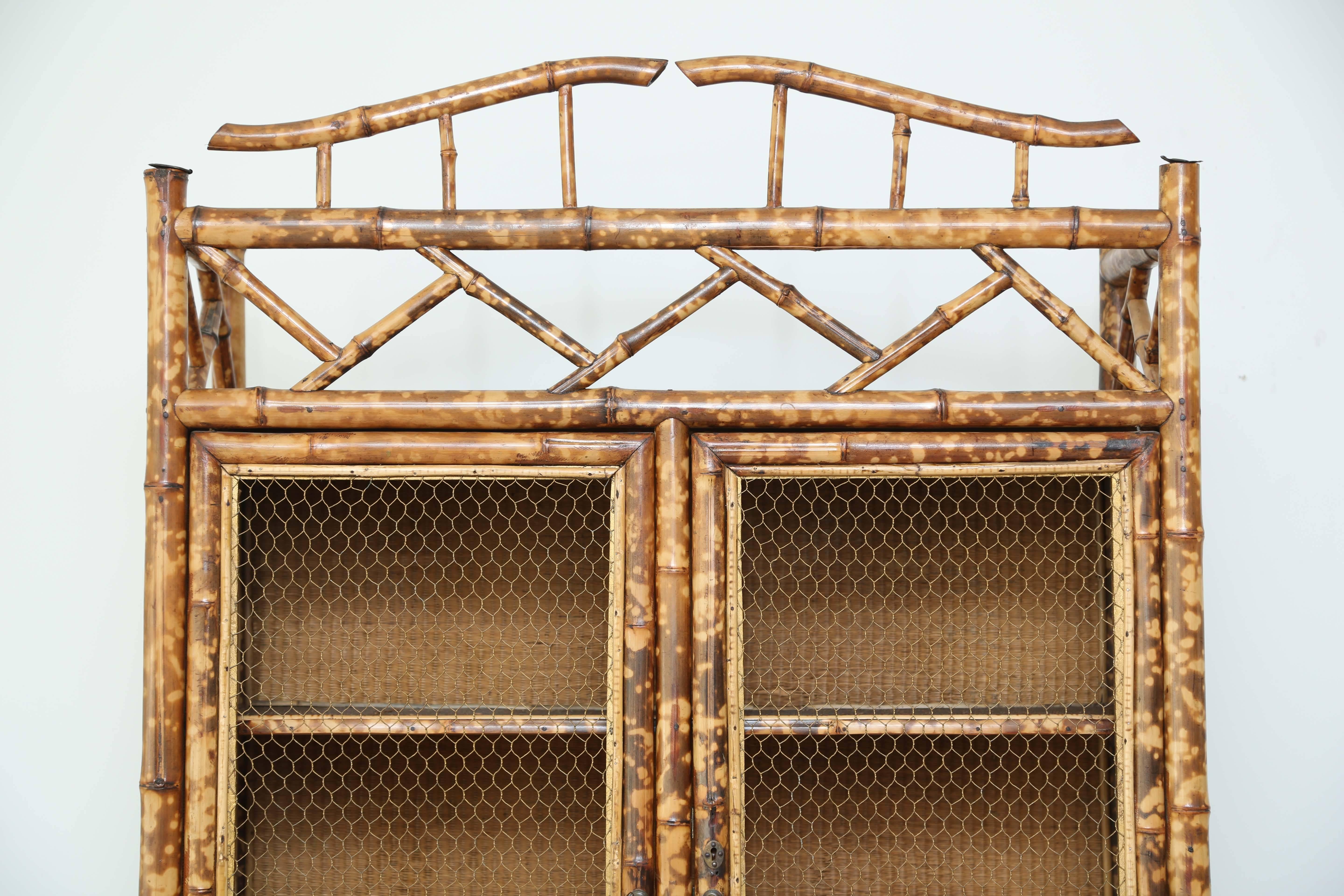 Lovely tortoise bamboo four-door cabinet. The top portion consists of two chicken wire doors with three shelves inside. The lower portion also consists of two chicken wire doors and three interior shelves.
