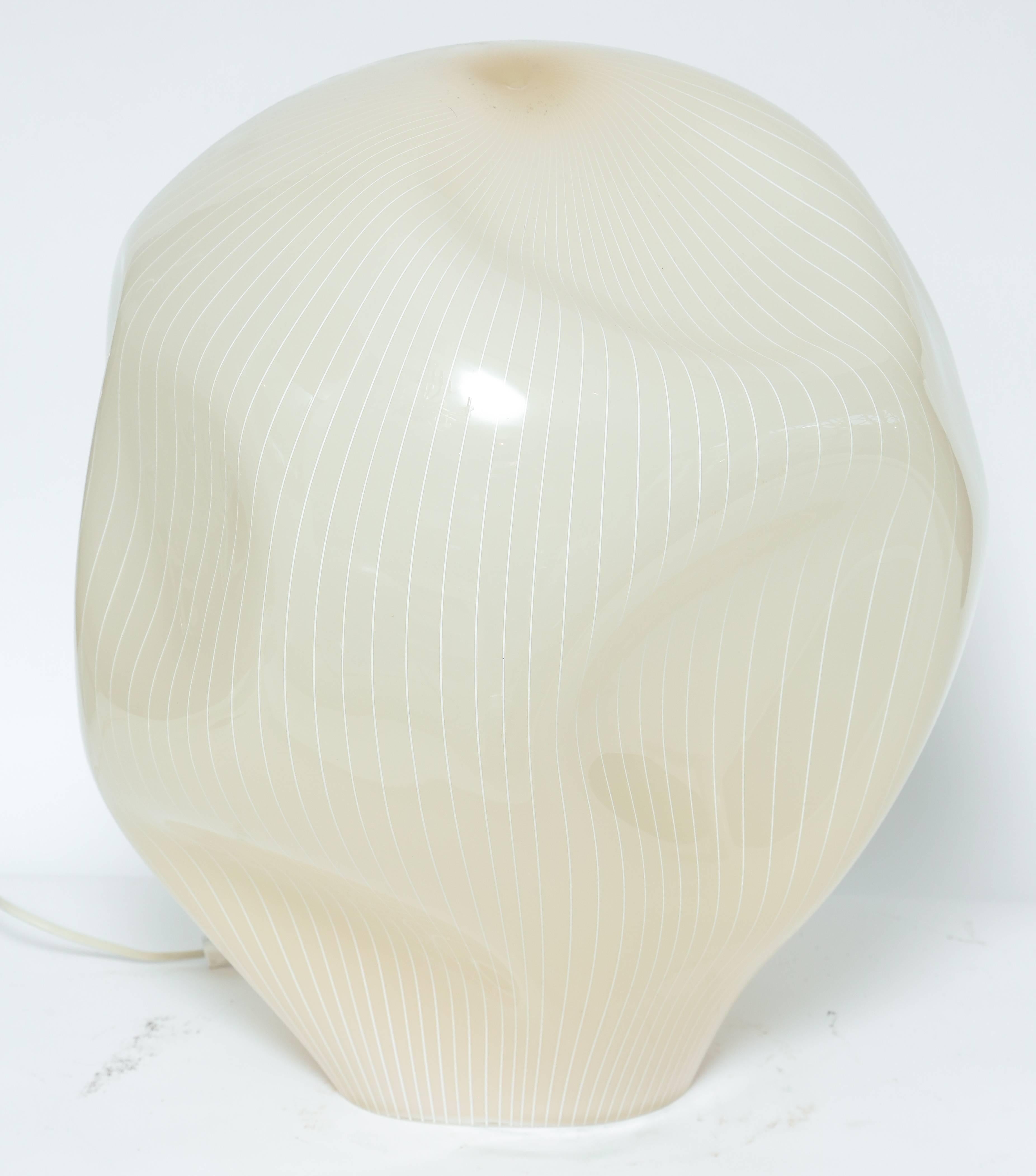 Handblown and designed by Gino Vistosi, this glass lamp is very sculptural. Soft amber color with white pin stripes this lamp emmits a warm glow. In excellent vintage condition this lamp uses a regular bulb. Wiring original and in working order.