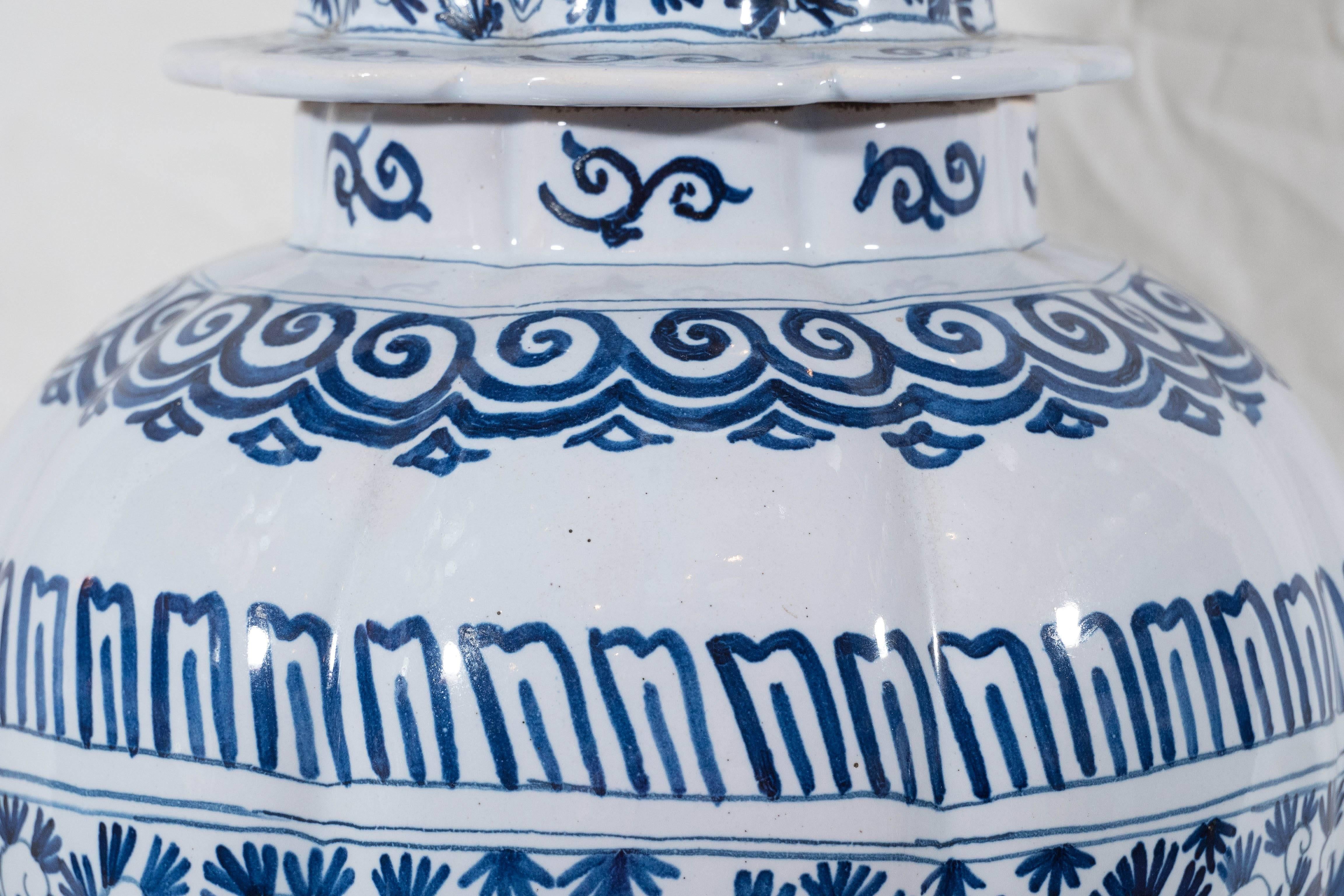 A pair of Dutch Delft blue and white covered jars. Painted with a lively pattern of flower heads, leaves and scrolling vines. The base, shoulders and cover decorated with bands of geometric designs. The cover with a lobed edge and traditional round