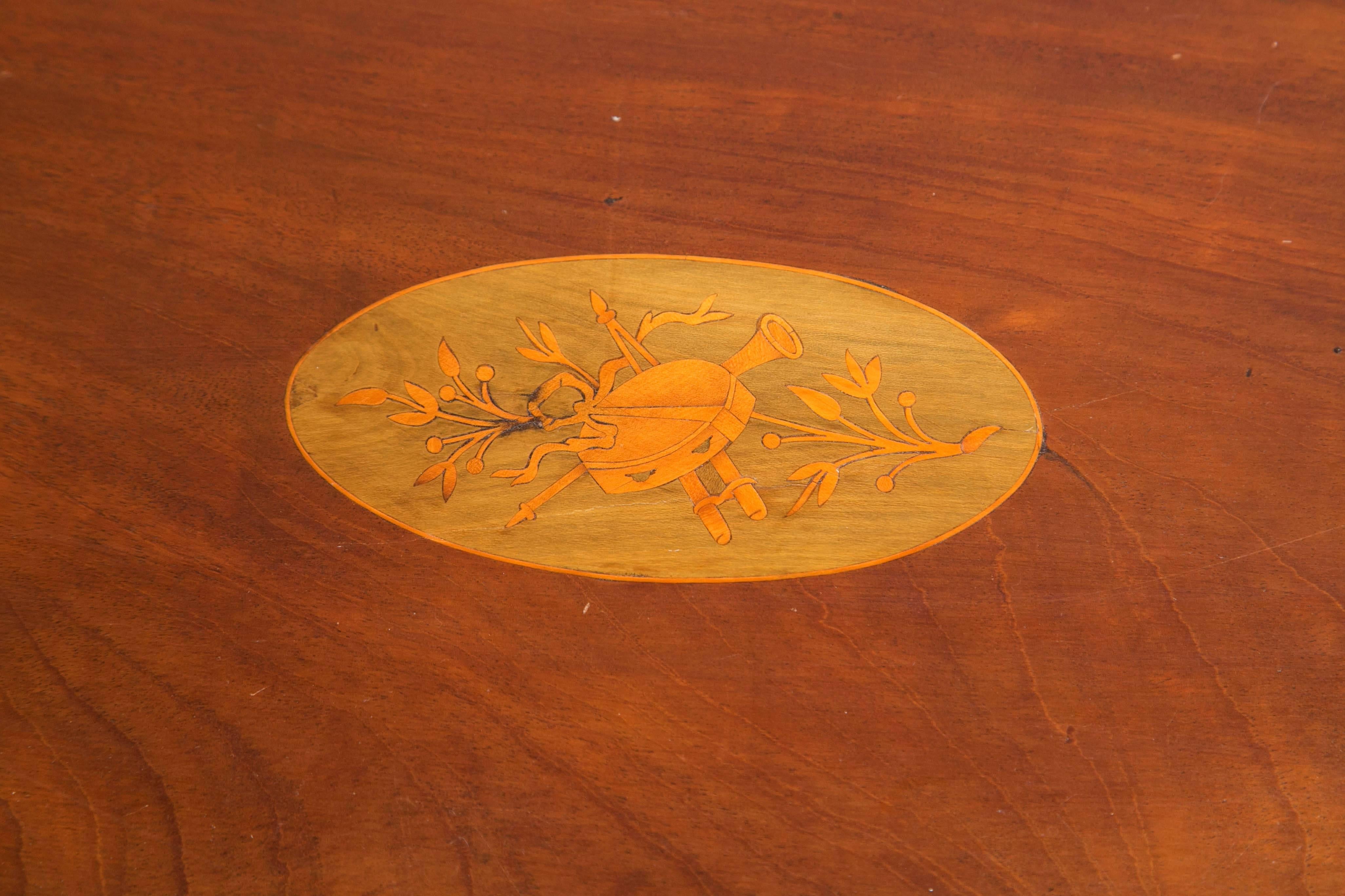 An ovoid form tray with two curved handles and a scalloped gallery rim on a felt lined oval Stand to create a low table. The center with musical trophies marquetry.