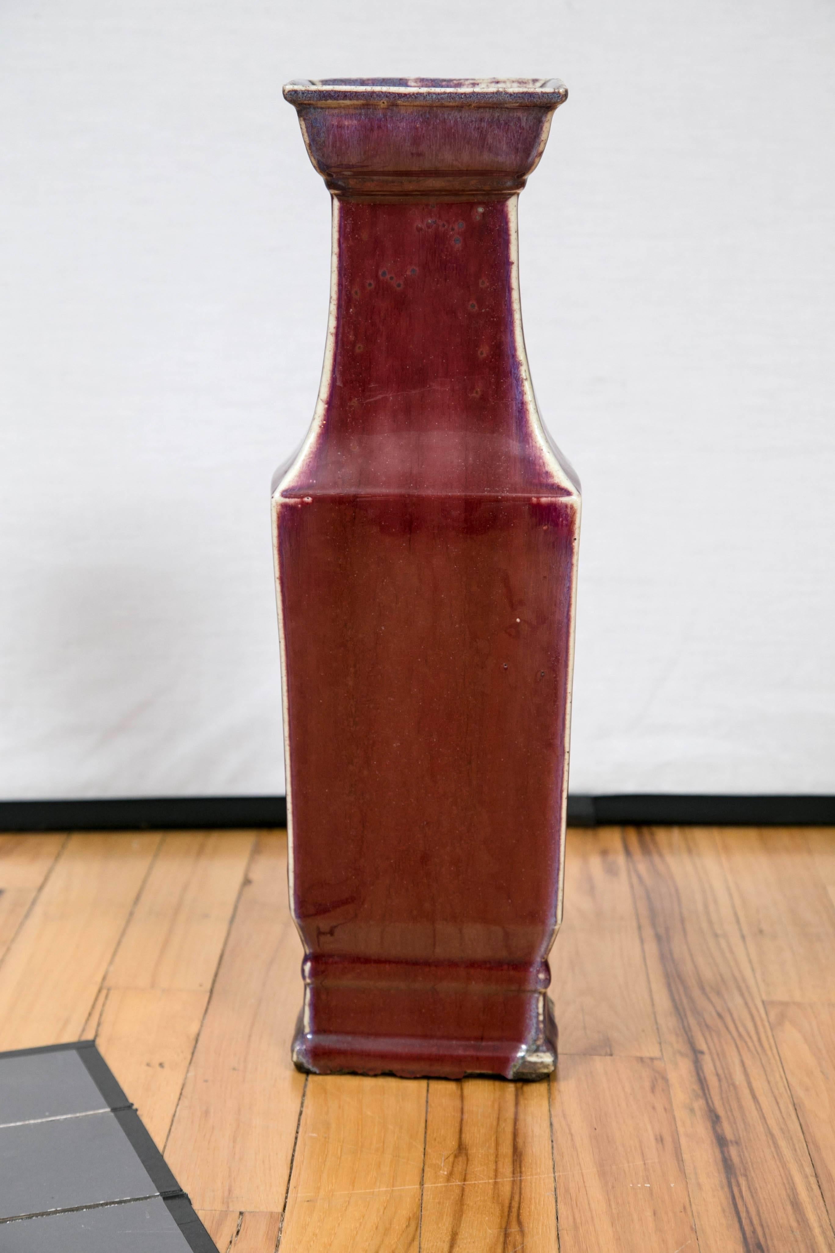 A tall square form oxblood glaze vase with tapering neck and rimmed foot.