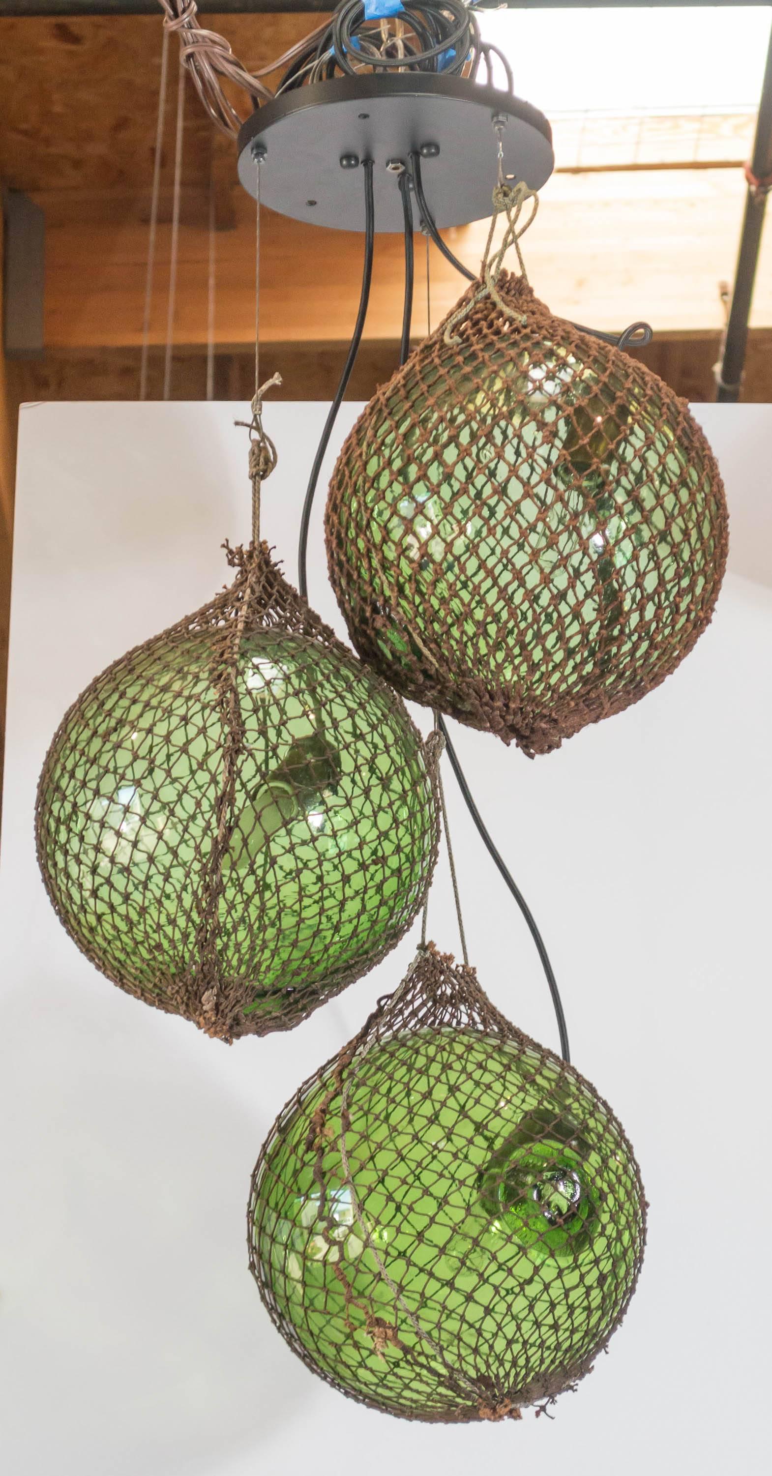 A pendant light made from three, large, green glass, float spheres
from Japan, with the original netting used for fishing. Newly fashioned with steel cables and bronze finished ceiling plate.  Height can be adjusted to be longer.