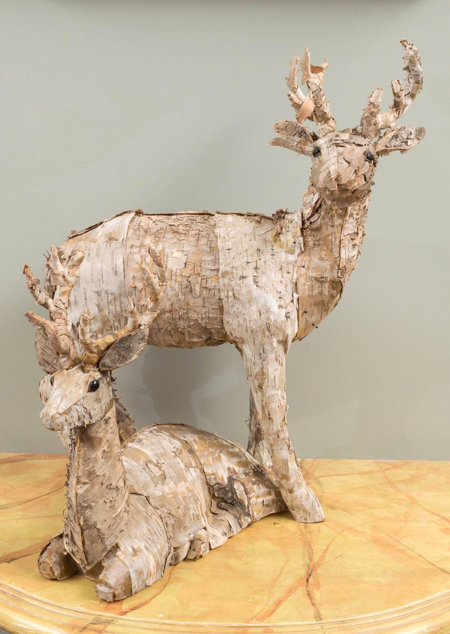 Each covered in birch bark with black eyes. The first, standing guard in an alert posture with outstretched antlers; the second, reposed in a relaxed manner.