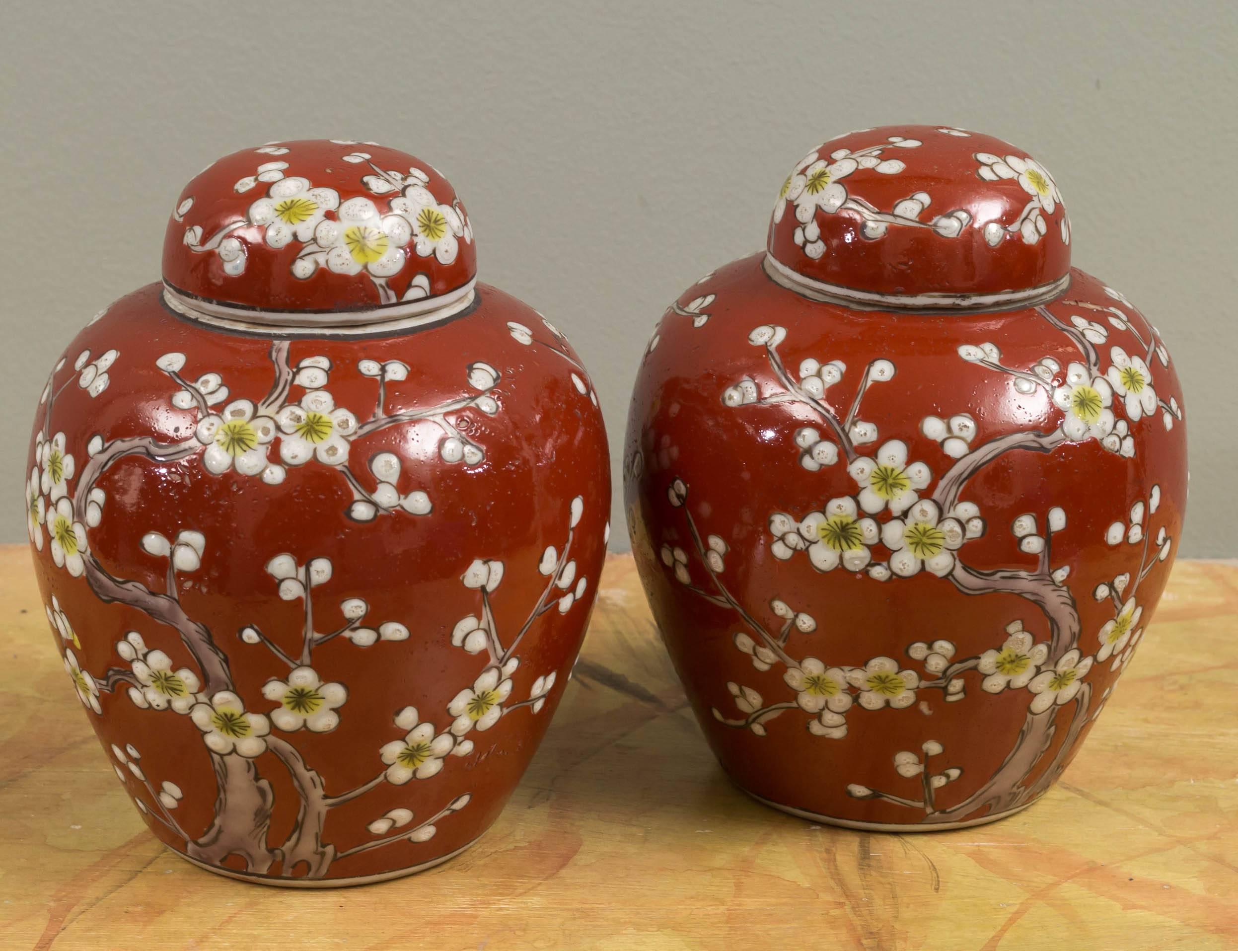 Each ceramic body and domical lid decorated with blossoming branches against a sanguine-colored background. With original import stamp on the base.