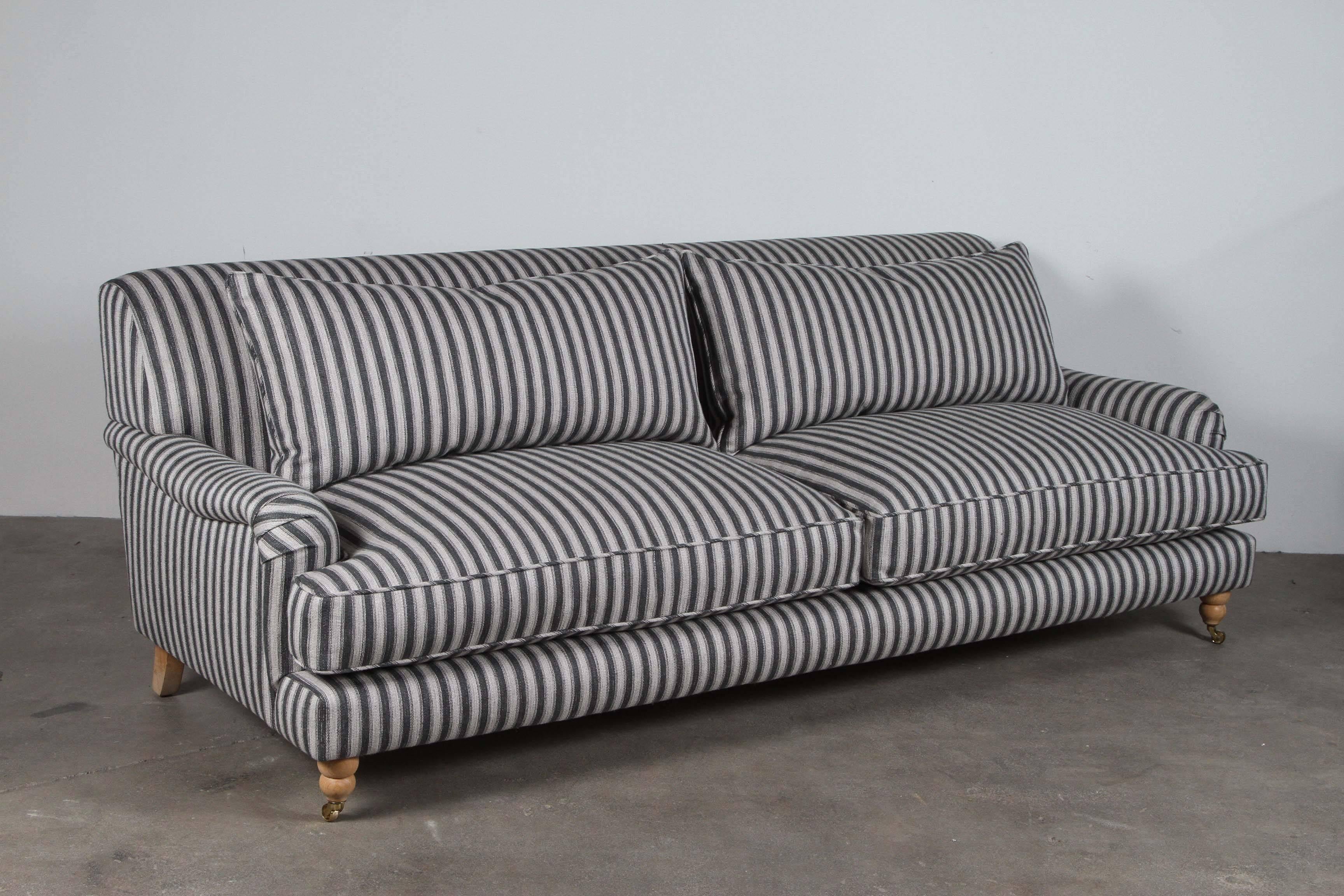 Traditional sofa newly upholstered in striped fabric. Loose cushion seat and back with rolled arms. Turned feet on casters.