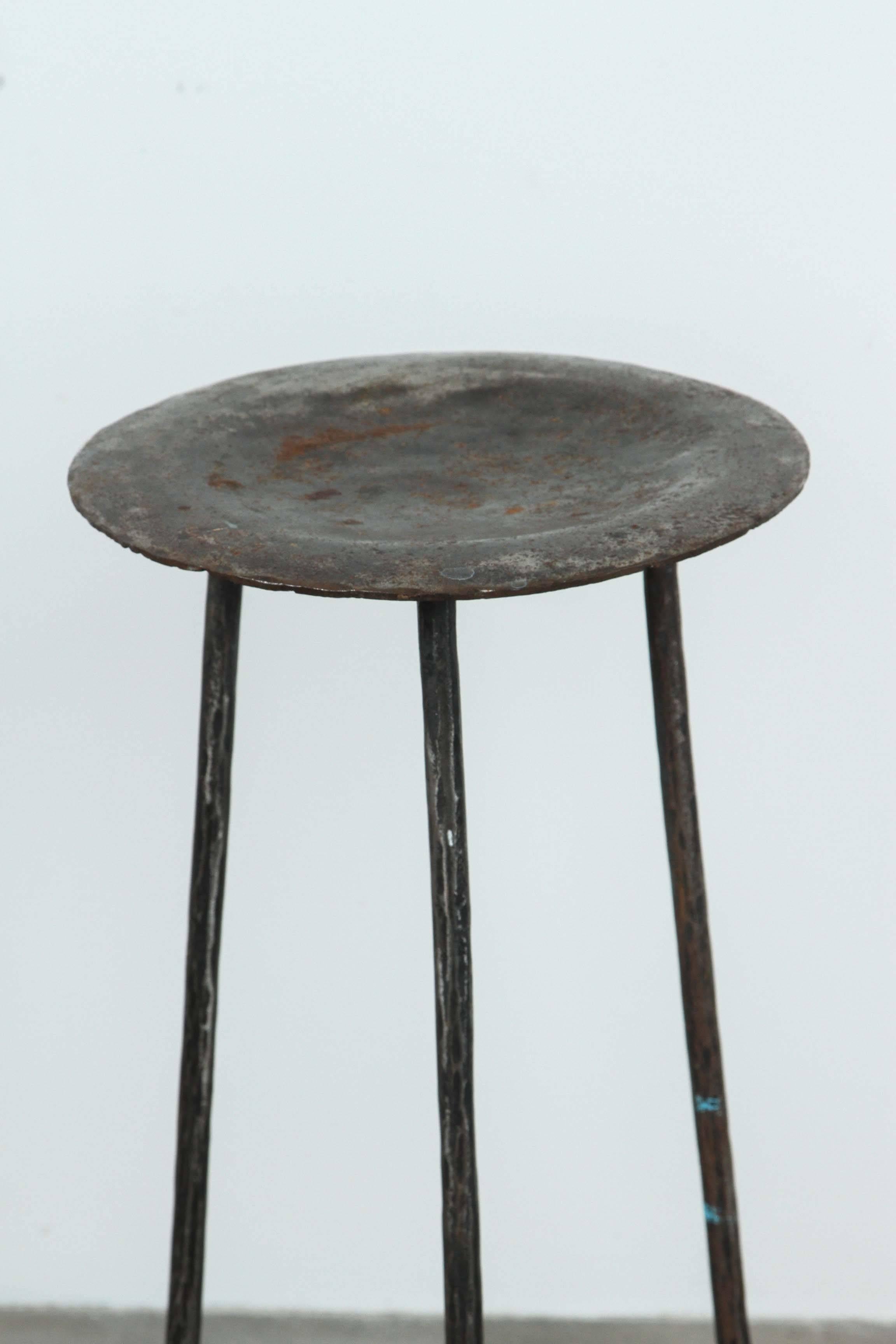 Three-legged tall slender iron stool.