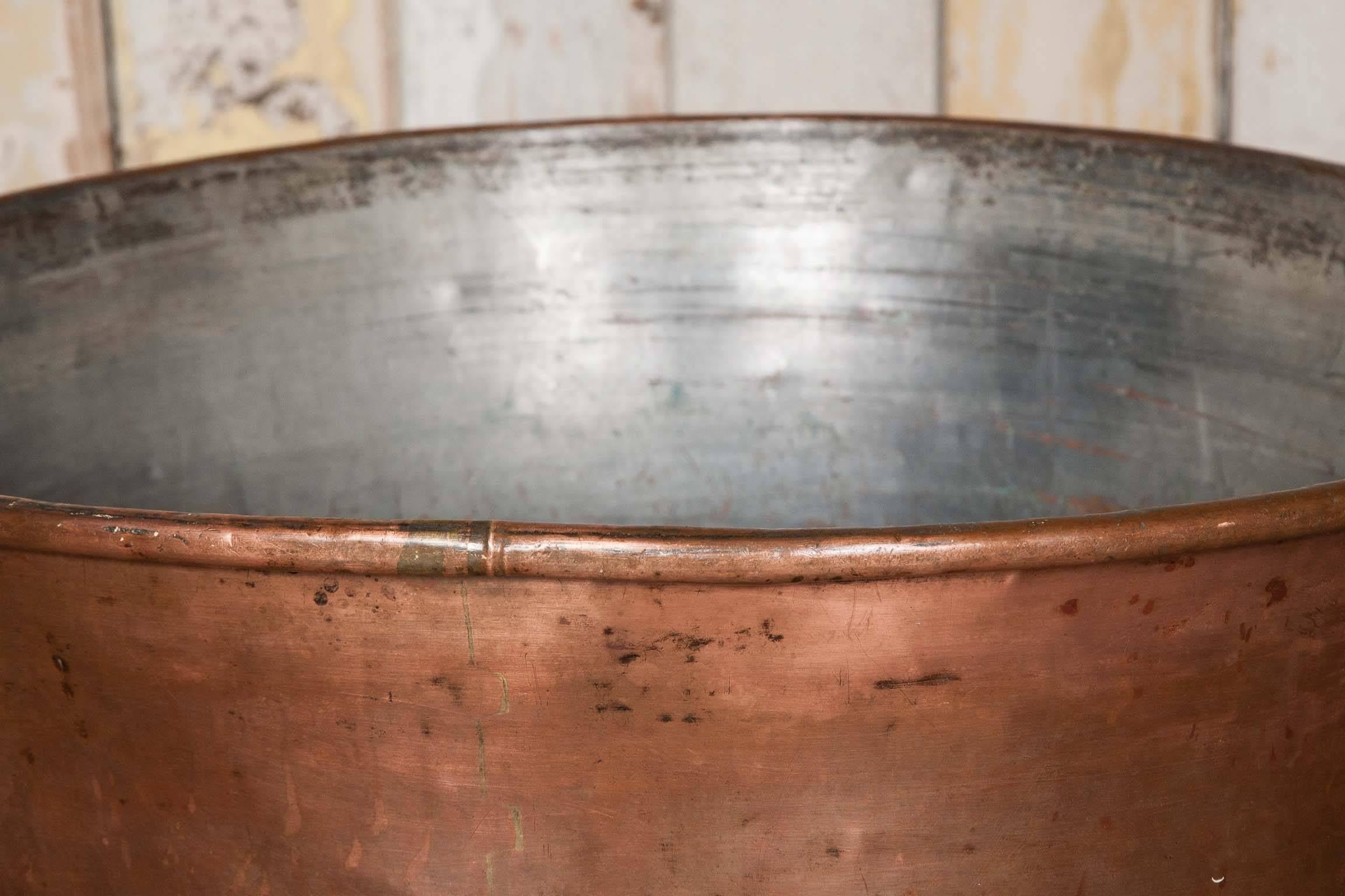An antique polished copper cooking pot. This large pot would have been created through beating thick sheets of copper into shape. This pot has two solid copper handles attached to the piece and has been given a polished finish.