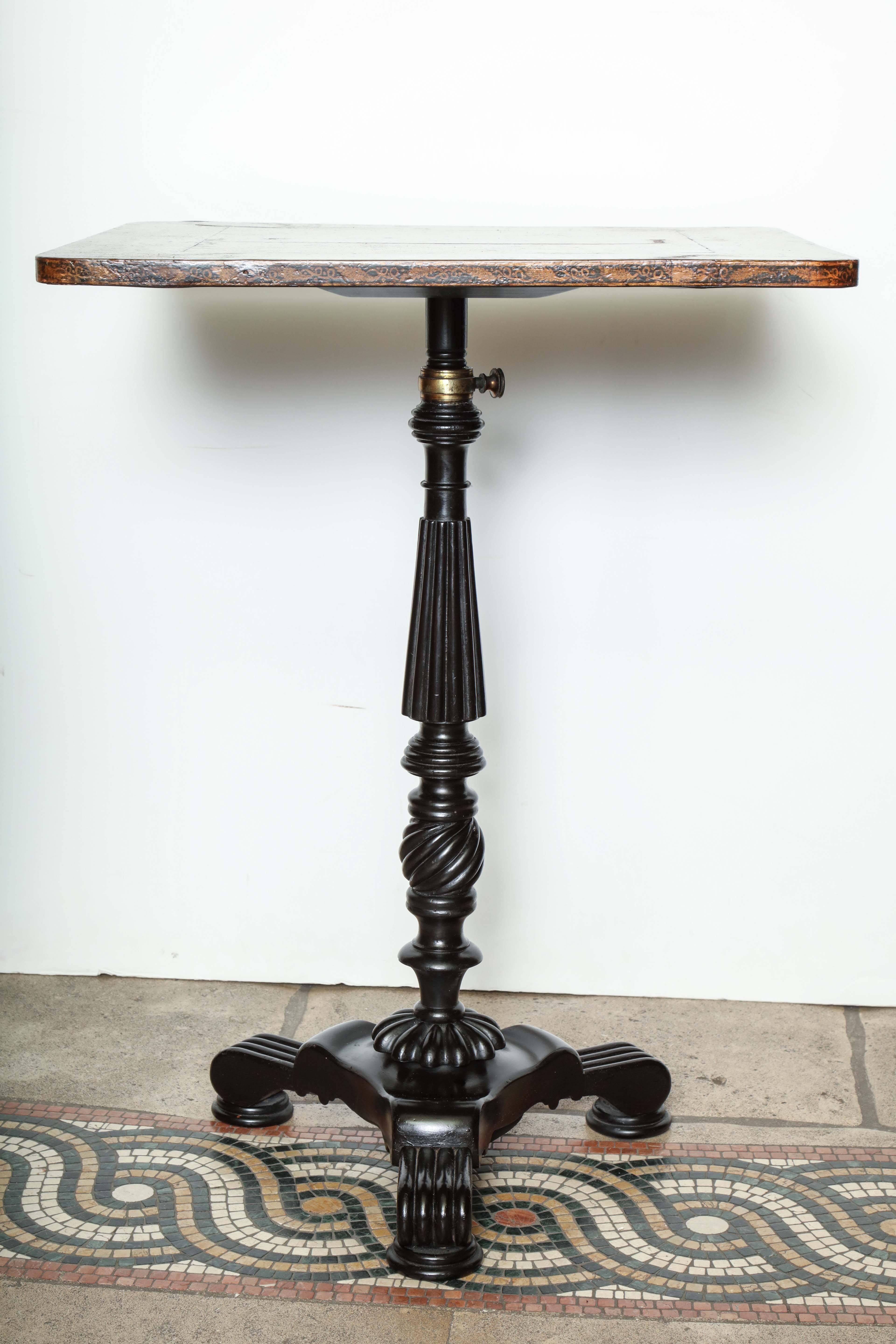 A penwork table having a height-adjustable pedestal base and a top surface decorated with animal and floral motifs.