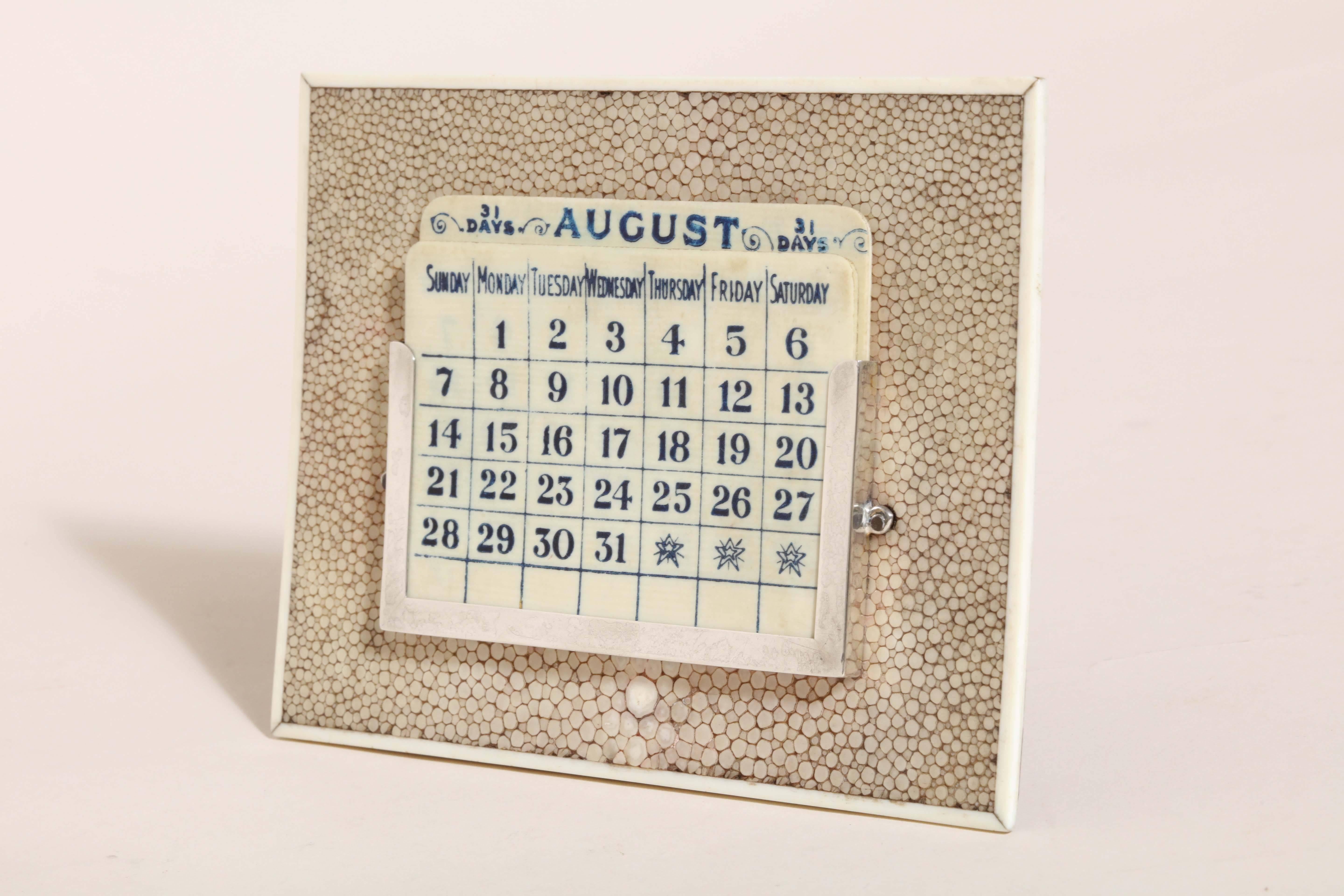 Perpetual calendar with month cards in sterling silver holder mounted on beige shagreen stand with bone border. All cards are present.

Impressed for 925 silver/ London/ 1924/ G B S.