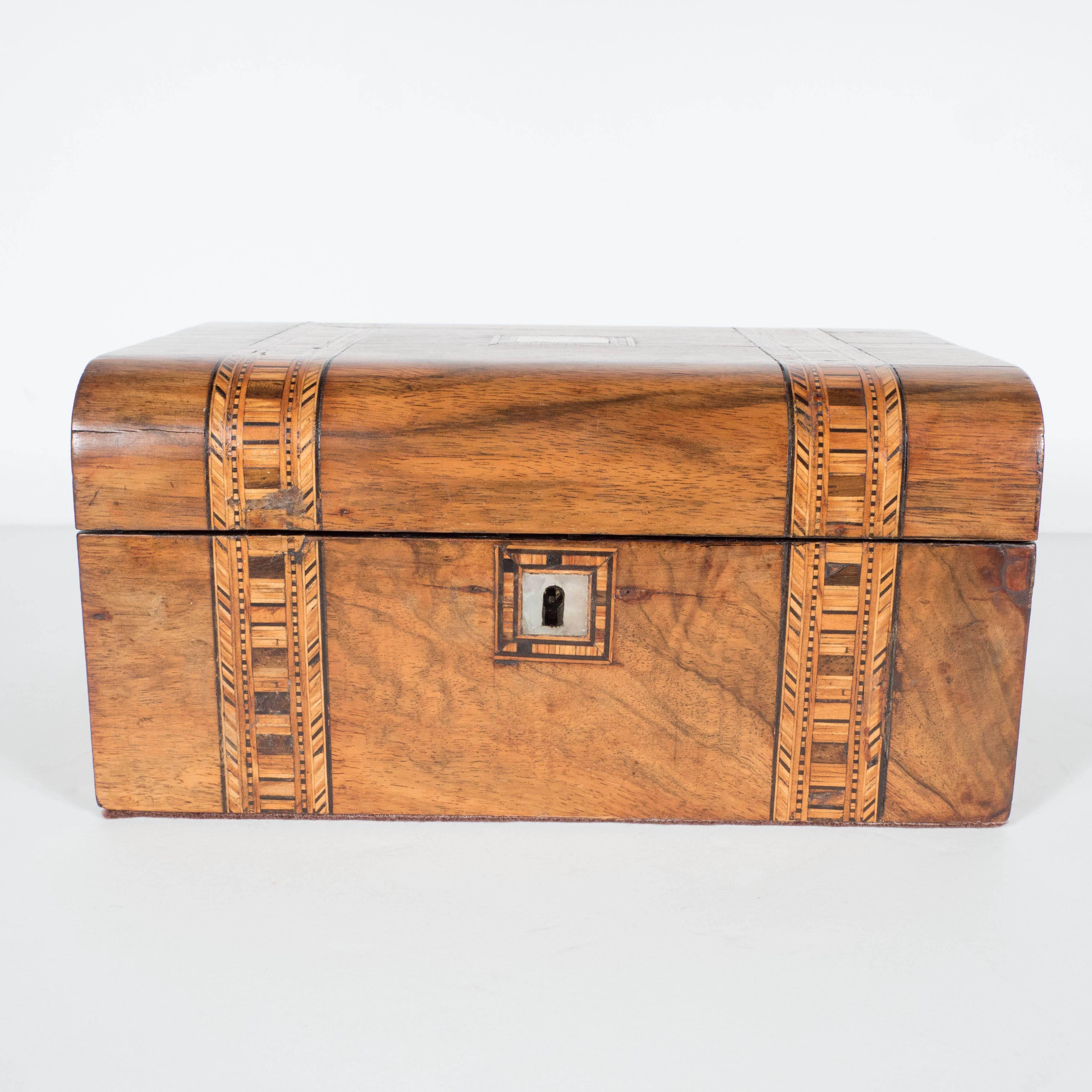 An intricately decorated Arts and Crafts wooden jewelry box adorned with two parallel bands of wooden segments. A central mother-of-pearl inlay is framed by more wood detailing. This piece comes with a working lock-and-key mechanism. The interior