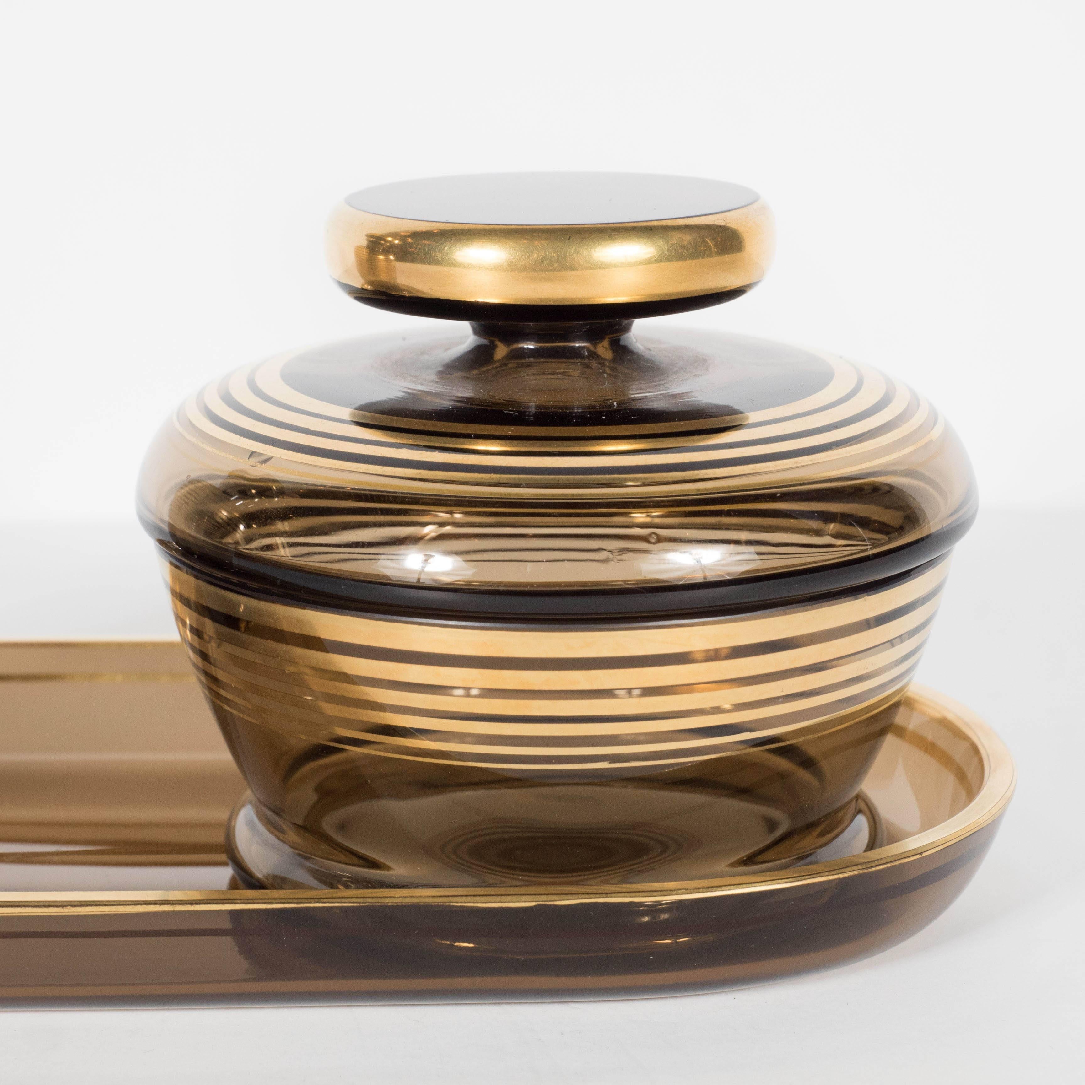 This stunning Art Deco dresser set features a tray, perfume bottle and covered box. Each of these pieces feature a streamlined 24-carat gold overlay lineal design of concentric rings. This is a wonderful example of the Art Deco period. It is in