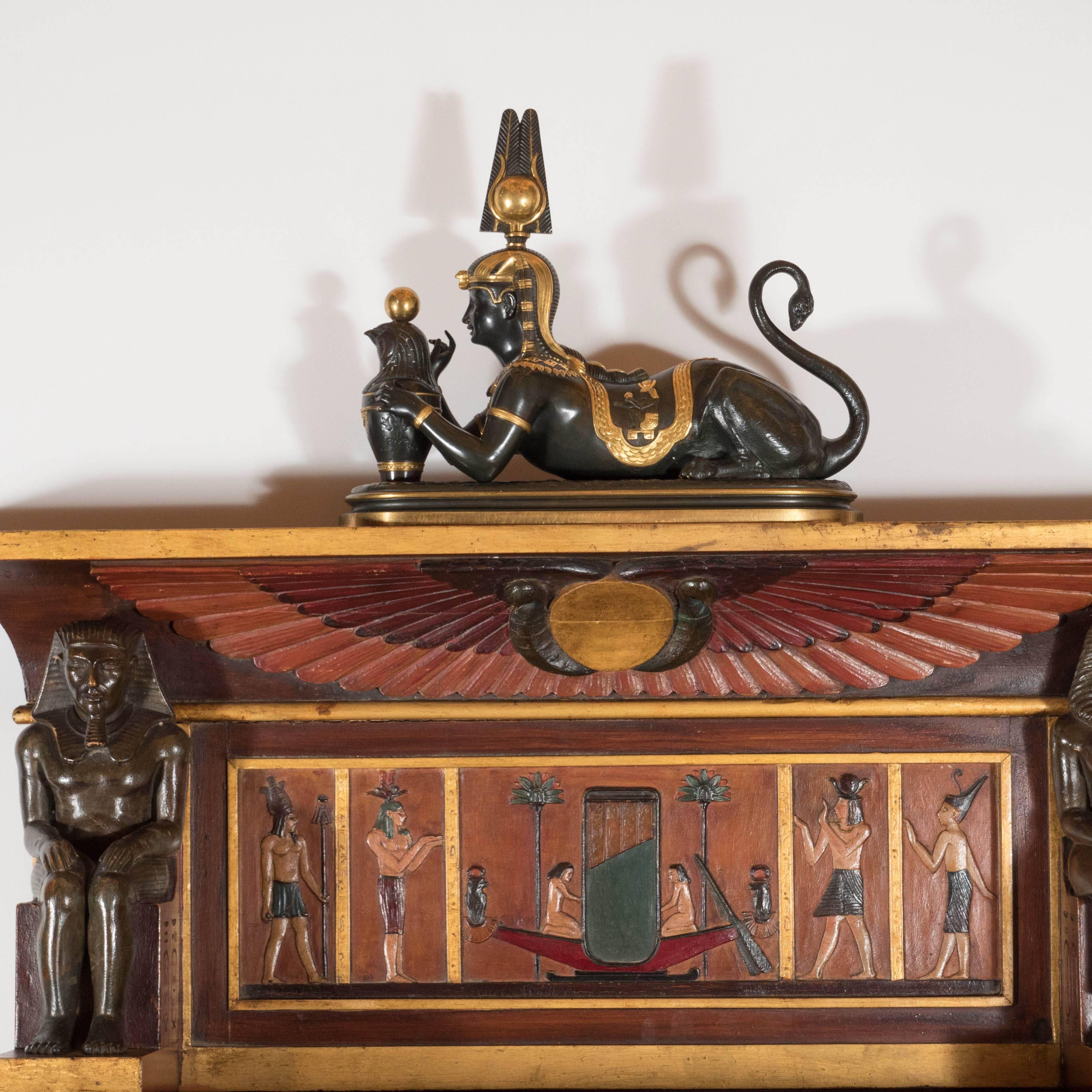 A very rare and detailed Art Deco Egyptian Revival pyramid secretaire with 24-karat gold leaf detailing throughout. A trapezoidal central section features a hinged drop-down panel which depicts horse and chariot scenes with surrounding workers.
