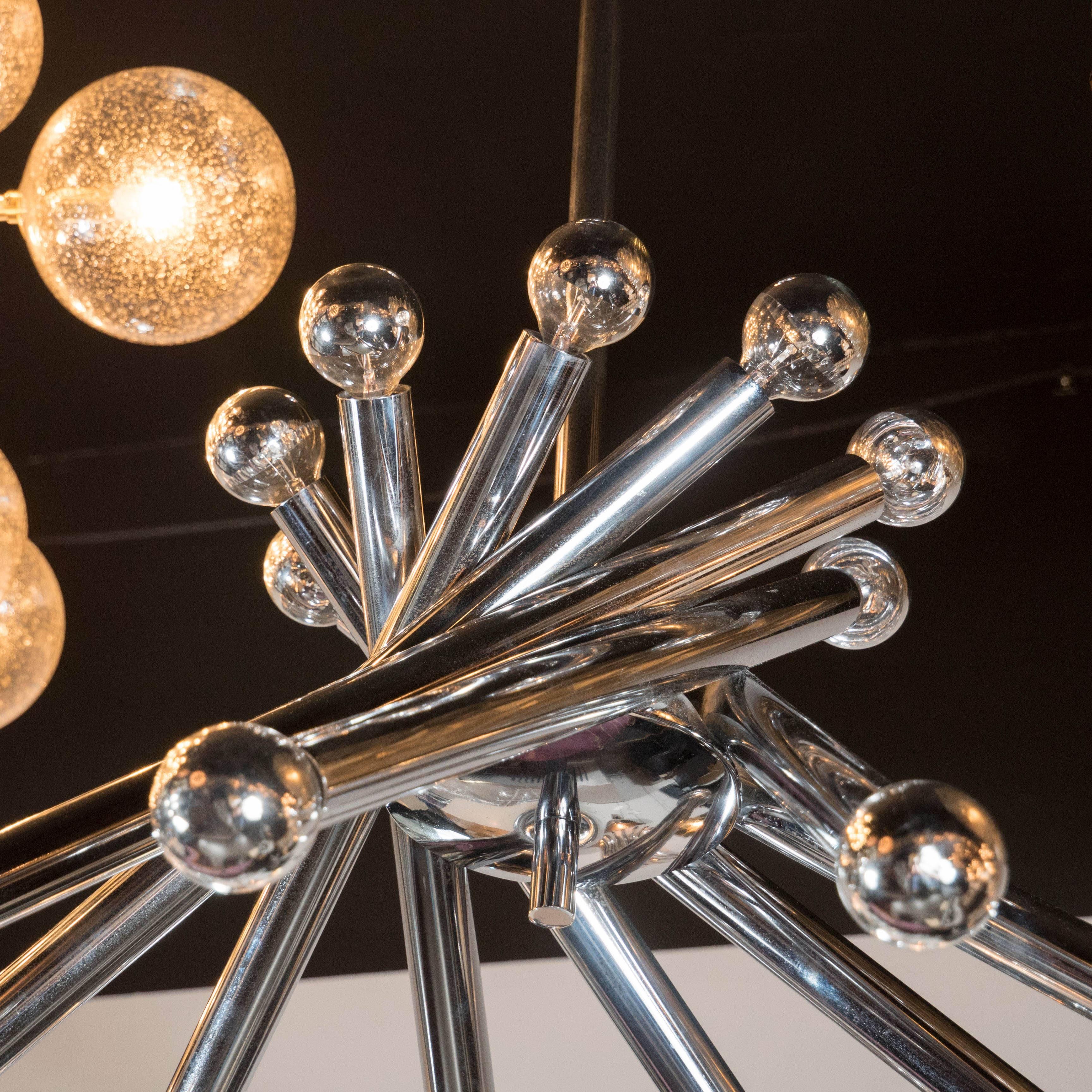 A Mid-Century tubular chrome chandelier in the manner of Gaetano Sciolari. A central chromed dome supports a pinwheel of chrome tubes, each supporting two chrome-dipped bulbs, totaling 18 in all. A chrome rod supports the piece. It has been