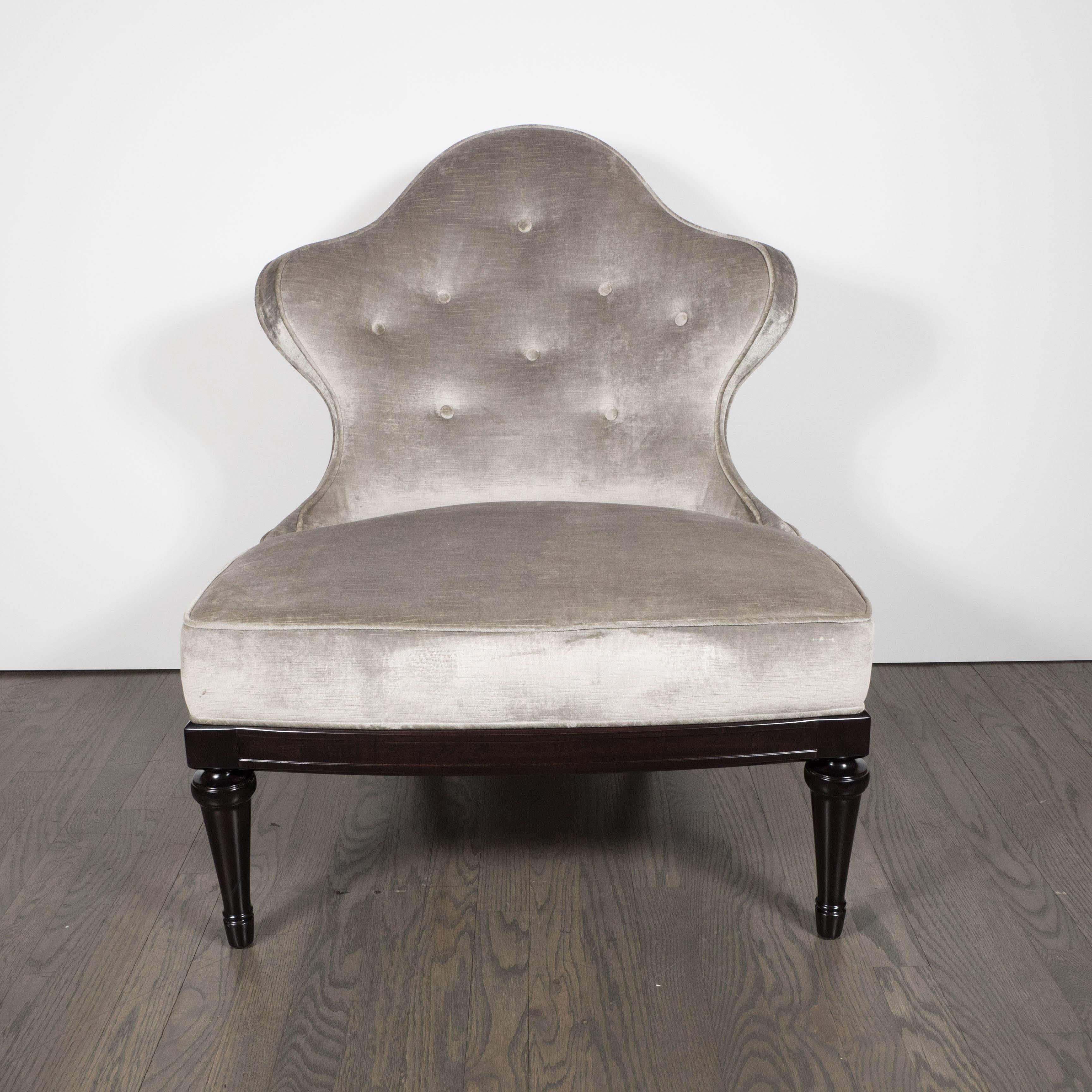 A 1940s Hollywood Regency crest-back button-tufted slipper chair in platinum velvet. Detailed legs and base in lacquered ebonized walnut support a button-tufted seat back and secured cushion. The piece is newly upholstered, piping included, in a