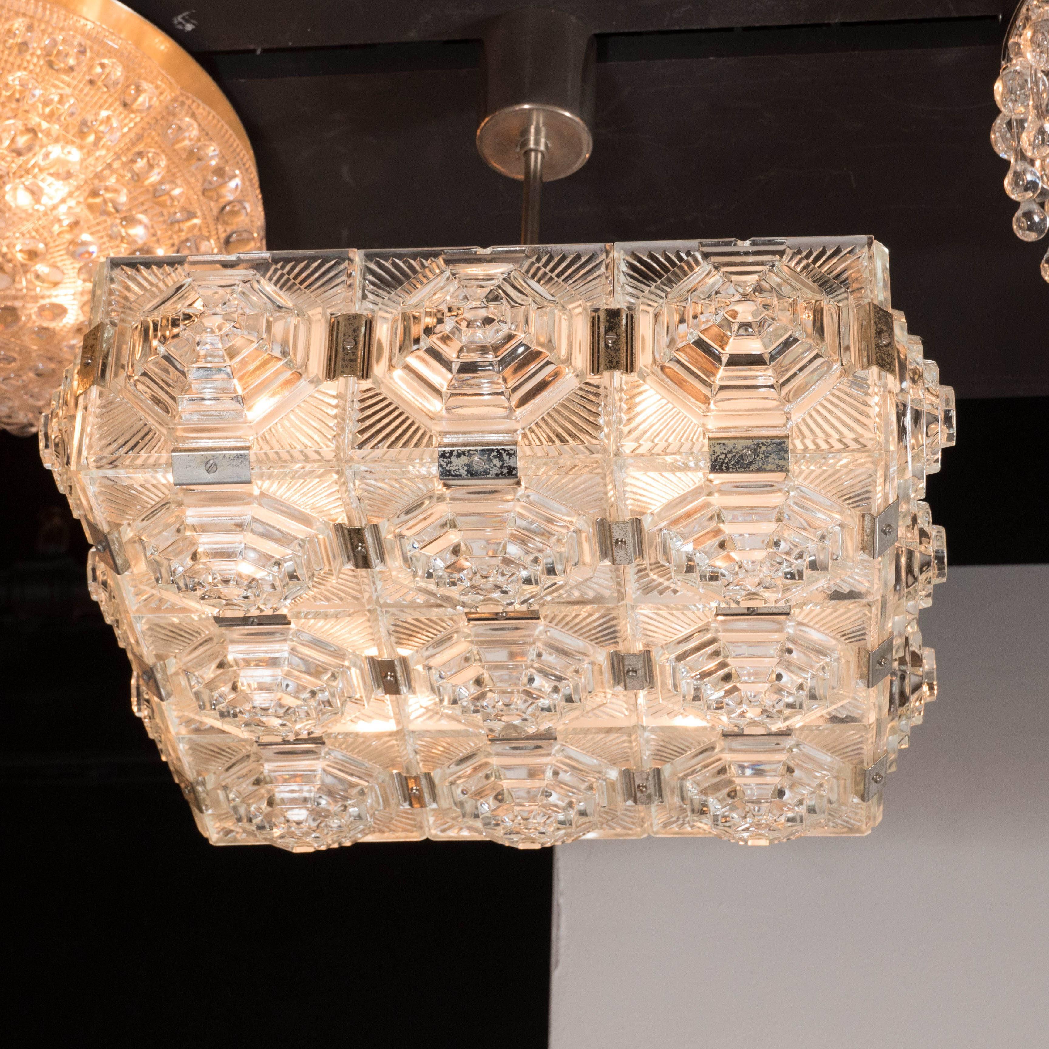 A Mid-Century Modernist semi-flush mounted chandelier in the style of Kinkeldey featuring a grid-like design of clear glass tiles with octagonal skyscraper style geometric patterns throughout. It is fitted with four candelabra bulbs (max 60 watts