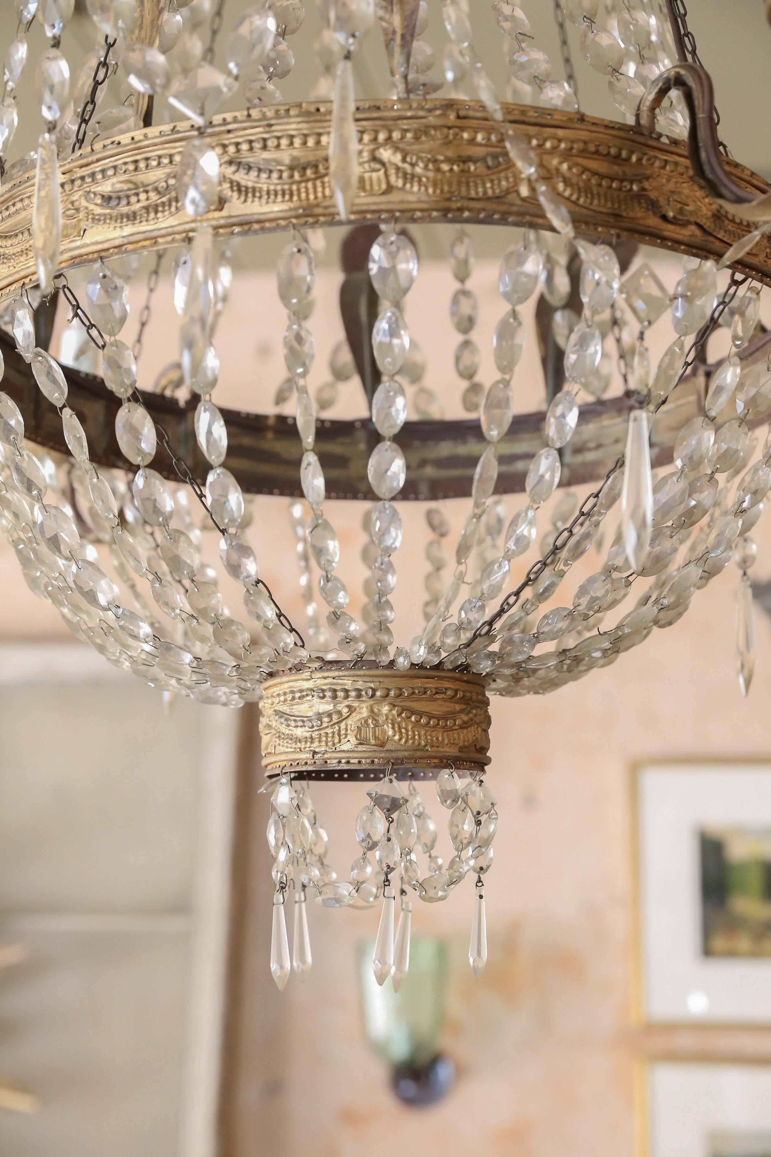 Italian Empire chandelier from Genoa in gilt repoussé tôle decorated in linked chains of crystal prisms and pendants. Extra chain, a canopy and mounting bracket updates this 19th century fixture, which is newly-wired for use within the USA.