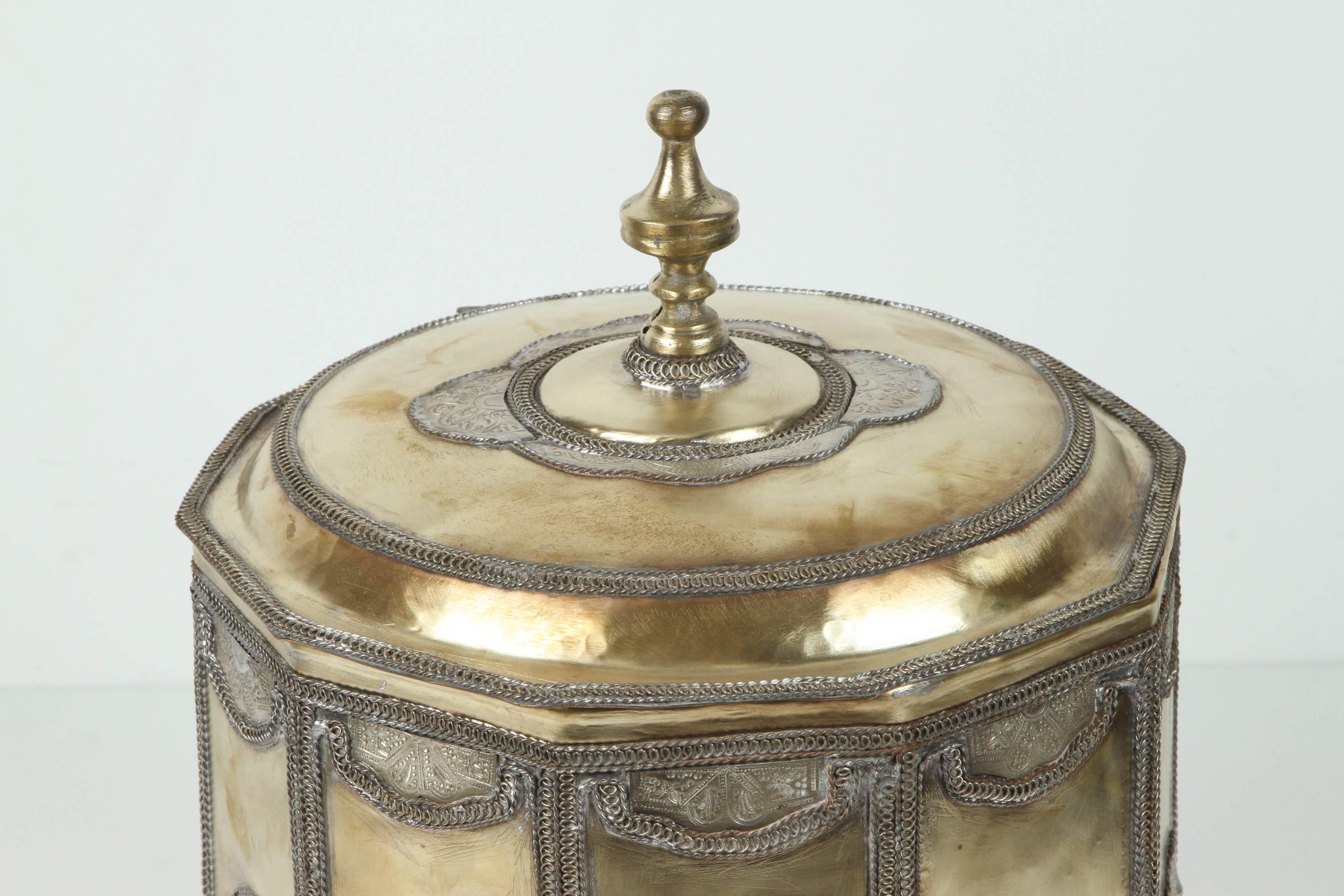 Large brass Moroccan footed cookie jar with filigree designs and hammered silvered round arabesque and Moorish decor.
Polished brass, handcrafted in Fez, Morocco by metalworker artisans.
