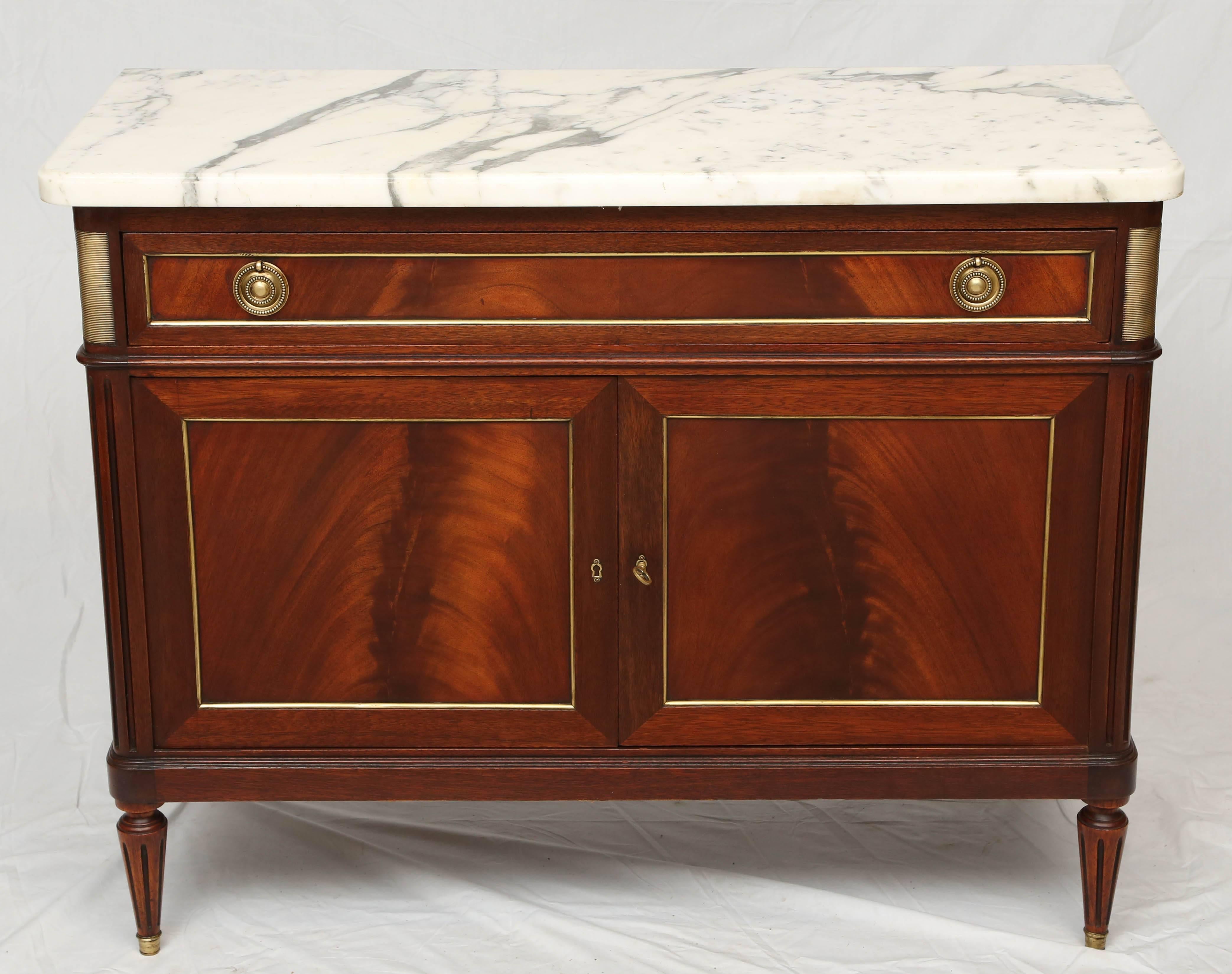 Fine Louis XVI enfilade, having a rectangular top of white marble, on a case of mahogany, of fielded panels, trimmed in brass, its single frieze drawer, over double cupboard doors, opening to interior drawers, flanked by ormolu headed, fluted