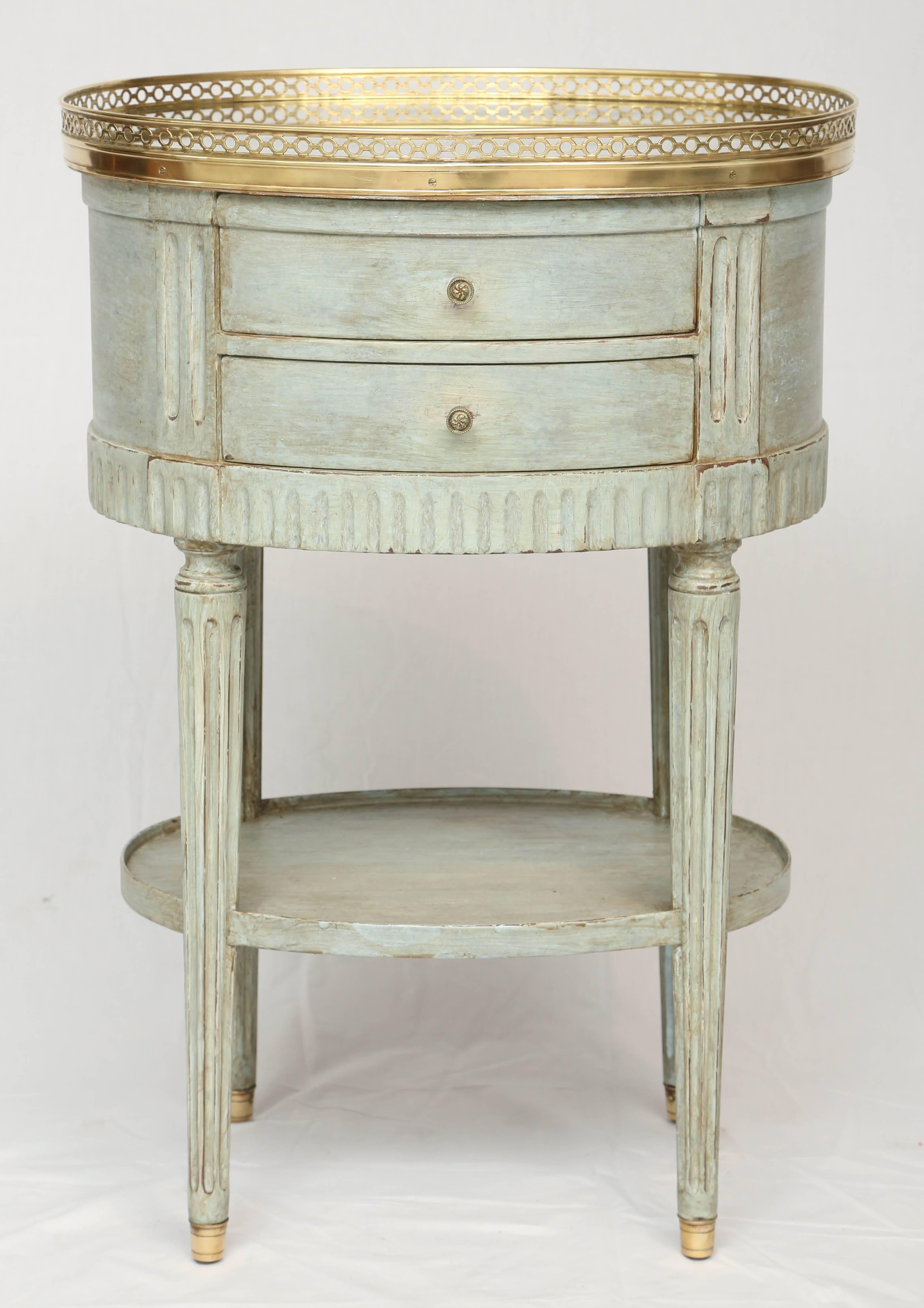 Side table commode, in the Louis XVI style, having an oval top of spotted mirror, bordered by pierced brass gallery, on painted table base, with fielded sides, double-stacked frieze drawers, raised on round, tapering, fluted legs, ending in cup