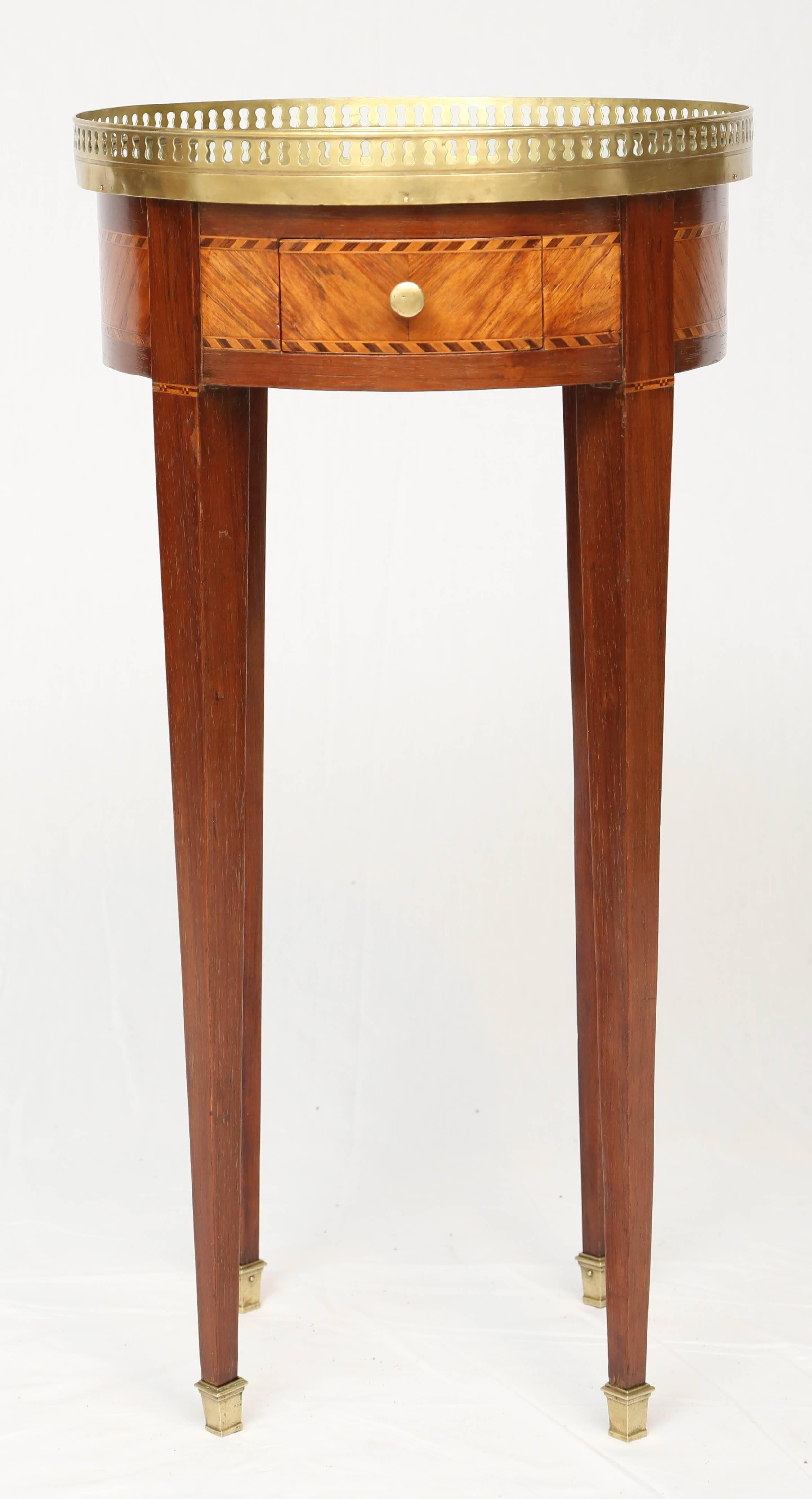 Small bouillotte side table, having a round top of distressed mirror, bordered by pierced gallery of brass, on table base of mahogany veneer, with parquetry decoration, single frieze drawer, raised on square-section tapering legs, ending in brass