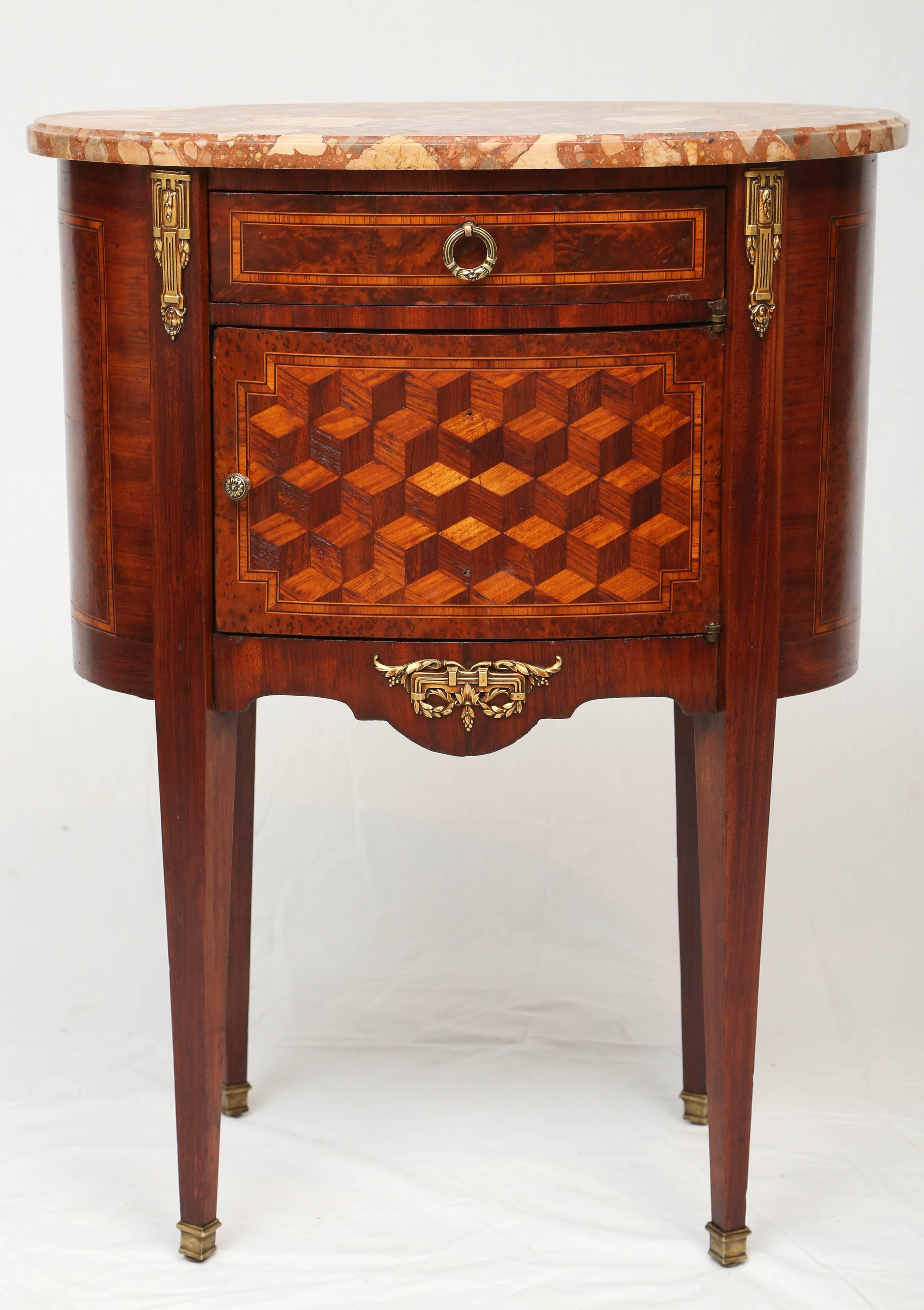 End table, having an oval top of breche marble, single frieze drawer framed in stringing, flanked by ormolu, over cupboard door decorated in geometric cube motif, shaped apron centered by classical ormolu, raised on square, tapering, legs, ending in