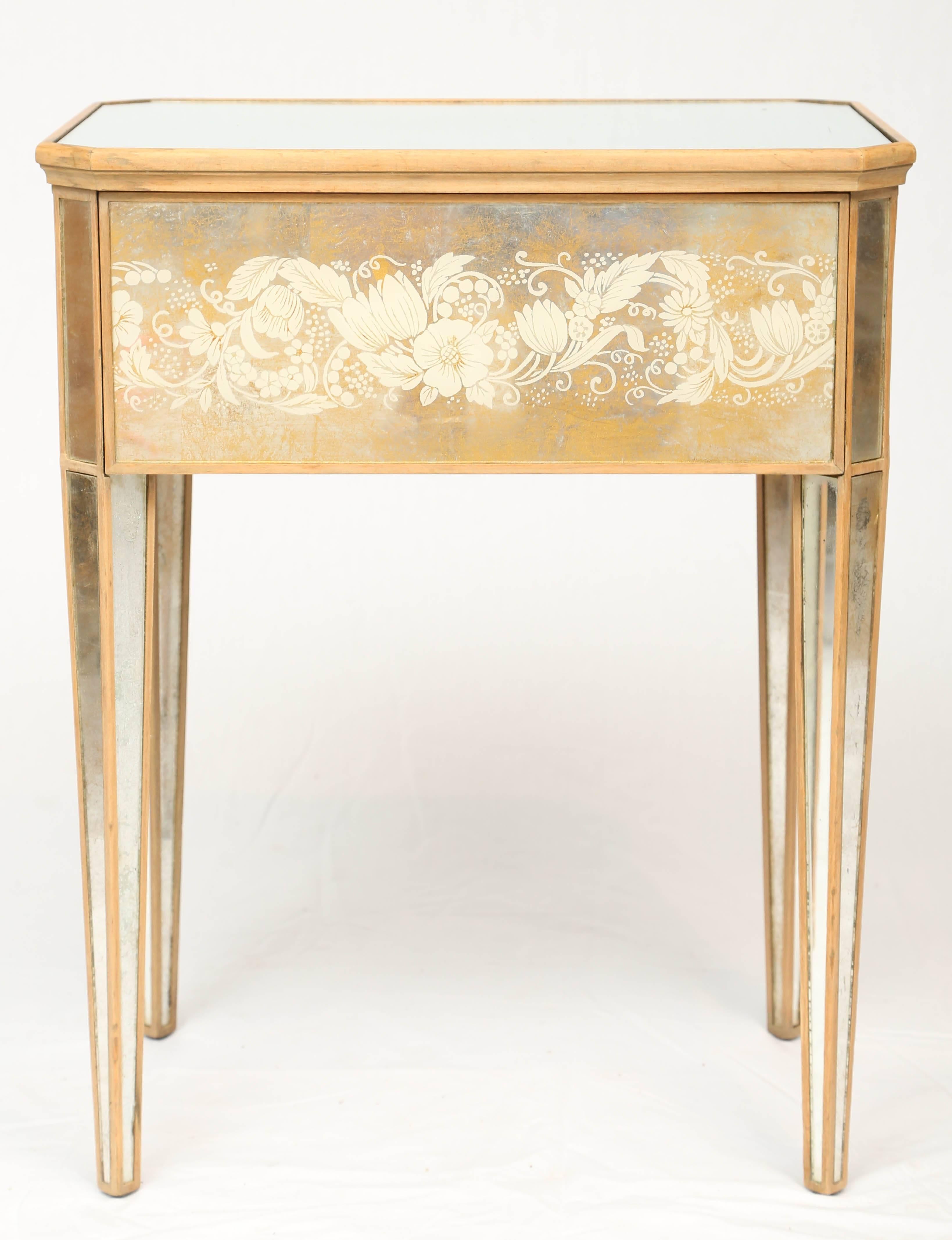 End table, having a rectangular top of mirror, with canted corners, on églomisé decorated apron, reverse painted with scrolling foliate, single frieze drawer, raised on mirrored, tapering square legs, on the angle.