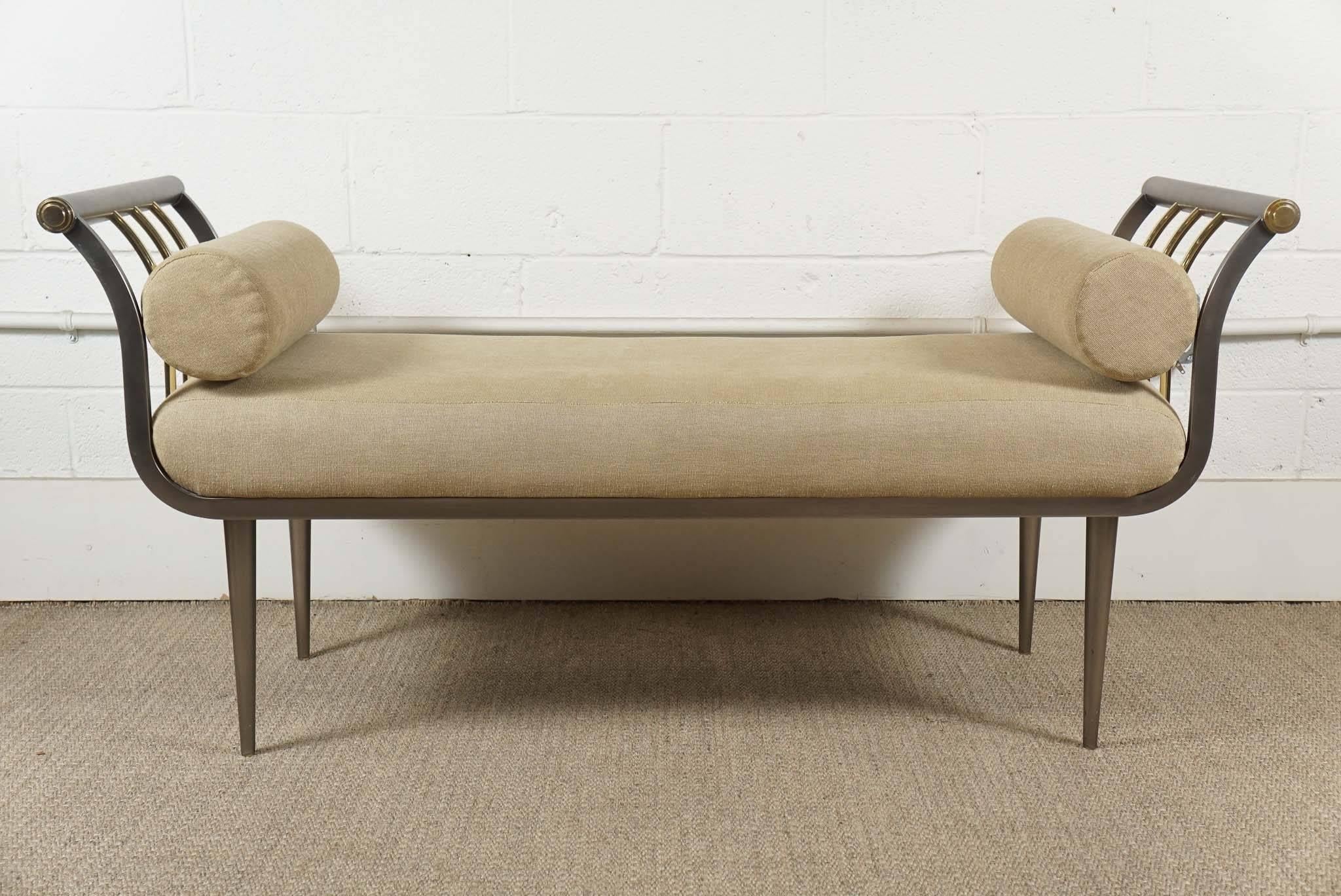 Here is a modern bench with elegant arms in a stainless steel finish and brass accents. The upholstered seat is attached and there are two bolster pillows.