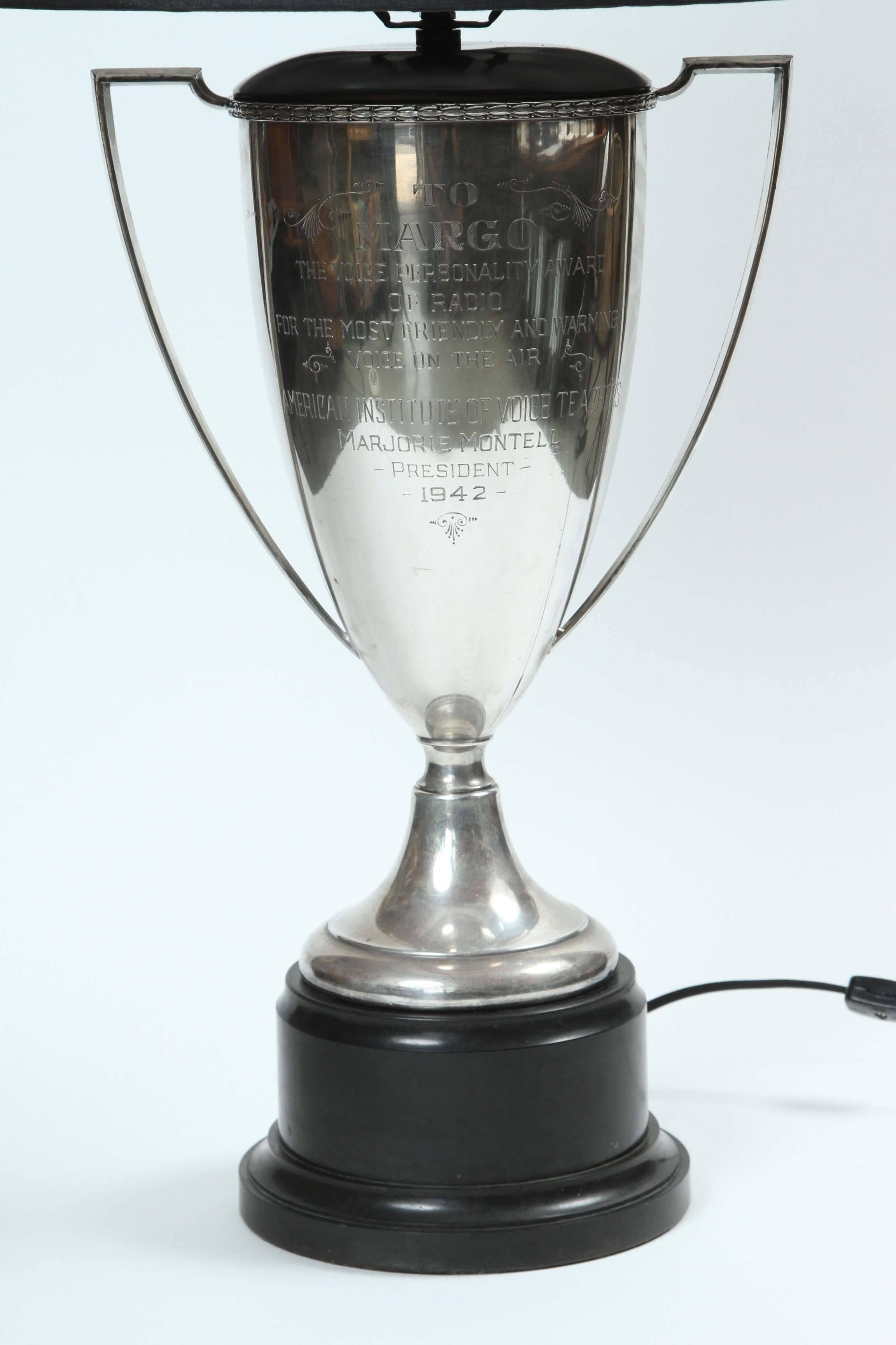 Engraved silver trophy from 1942 that has been newly made into a lamp with a custom black silk shade with silver lining. The base of the lamp is black and has a dimmer switch on the cord as well as on the trophy itself.