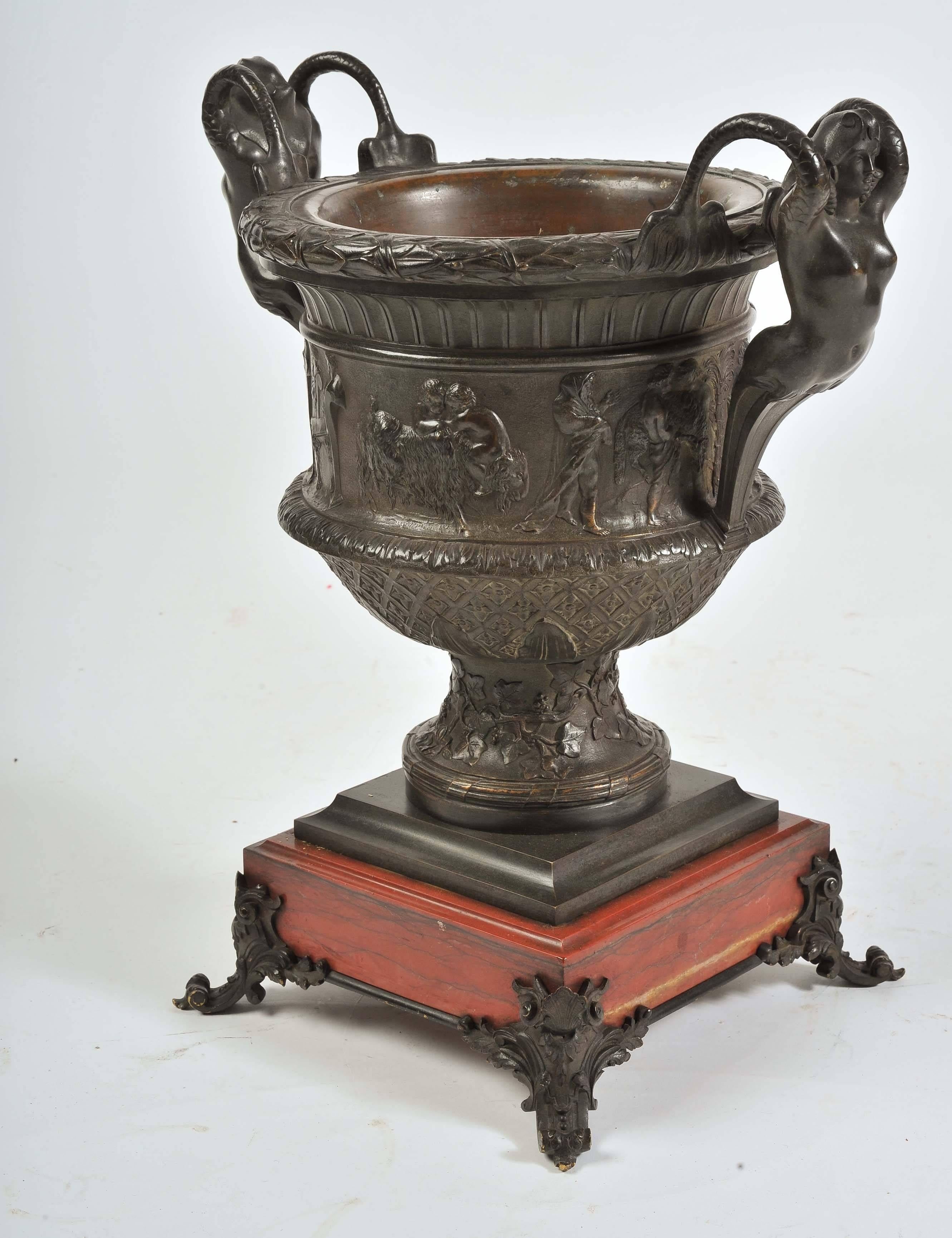 A very good quality French 19th century bronze two handled urn, having nude female figures to either side. Classical bacchus influenced scenes around the urn, foliate decoration to base and raised on a rouge marble plinth and bronze scrolling feet.