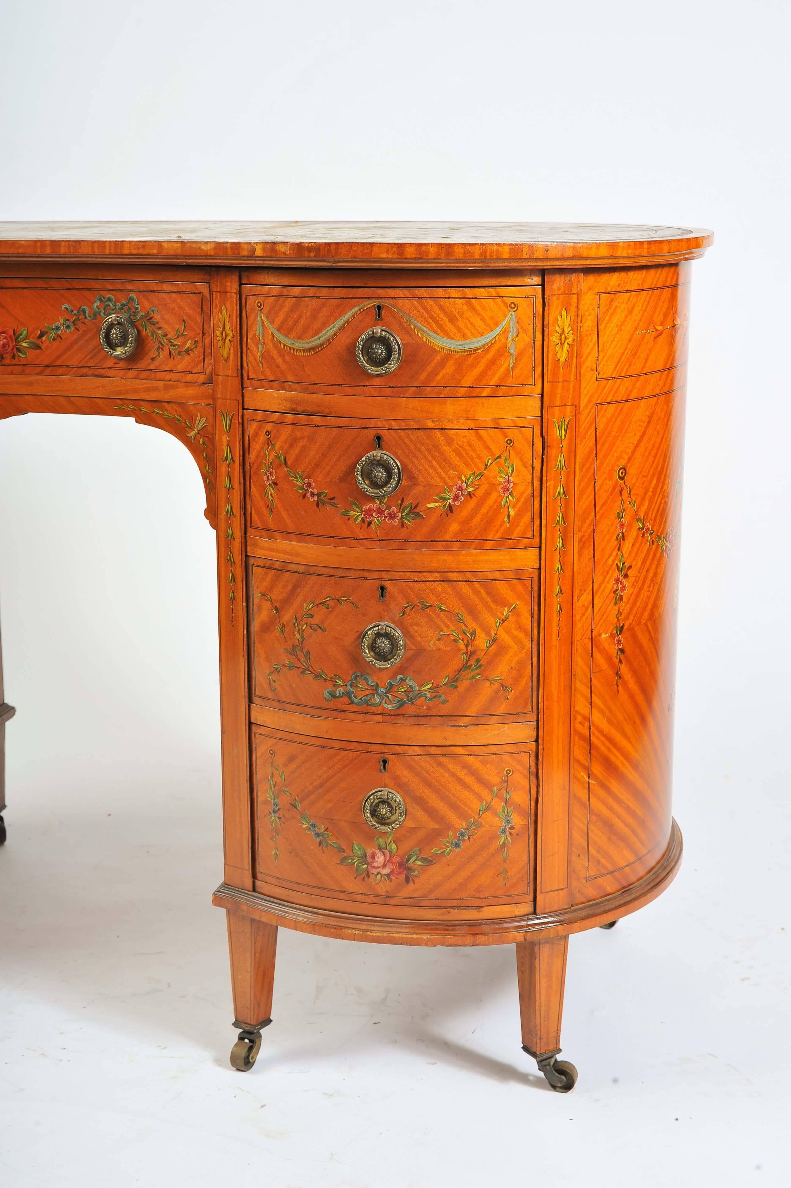 A rare pair of Edwardian satinwood, Sheraton revival kidney shaped desks. Having an inset leather tops, hand-painted classical swag and foliate decoration, nine mahogany lined graduating drawers, each with brass ring drop handles and raised on
