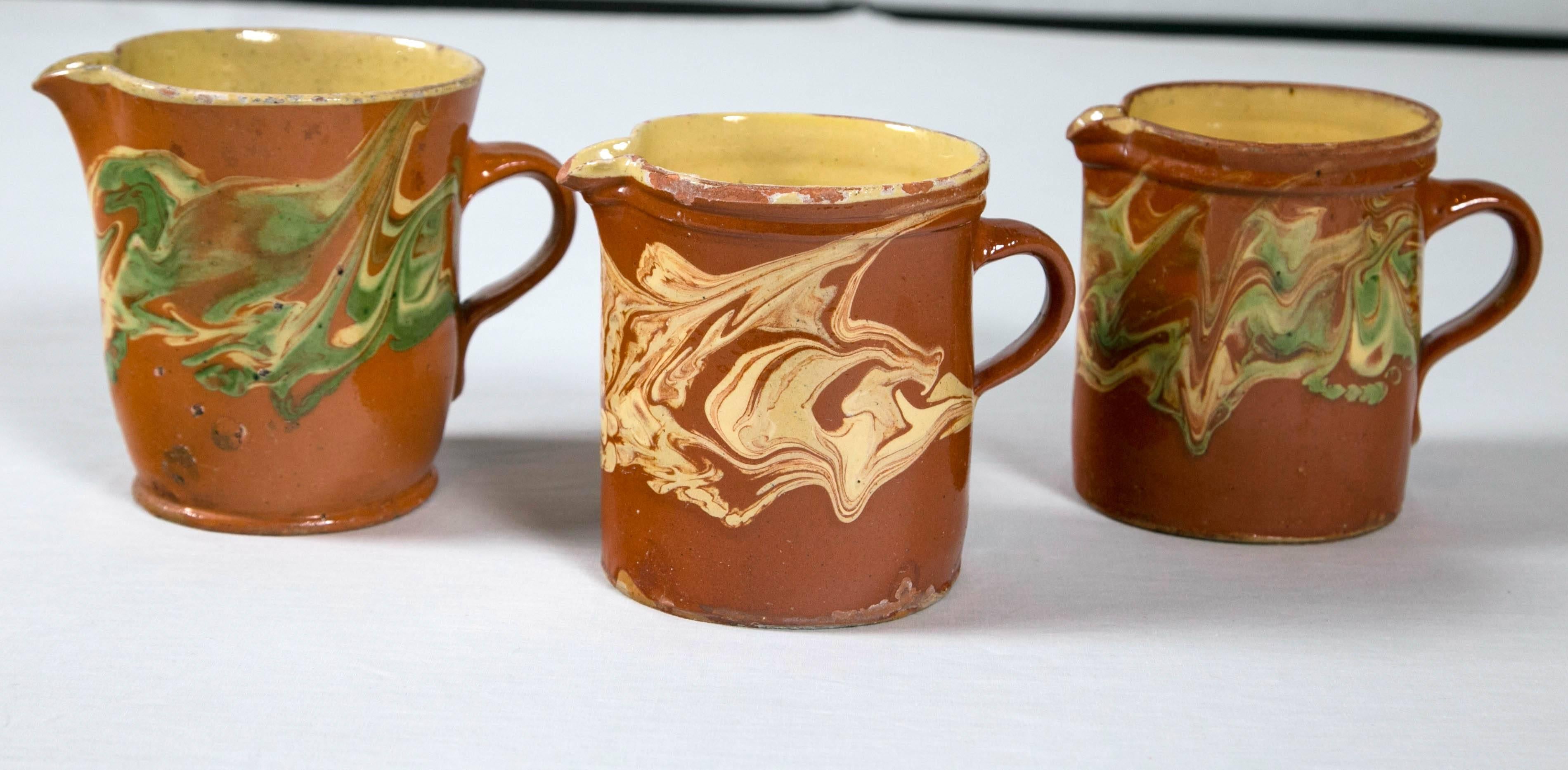 Three 'Jaspe' pottery pitchers from Alsace, France, circa 1900. Beautiful pale green and yellow swirl designs. Yellow glazed interior. Unglazed bottom indicating age. Size range: Height - 5-1/2 to 6 inches, Width - 4-3/4 to 5 inches.