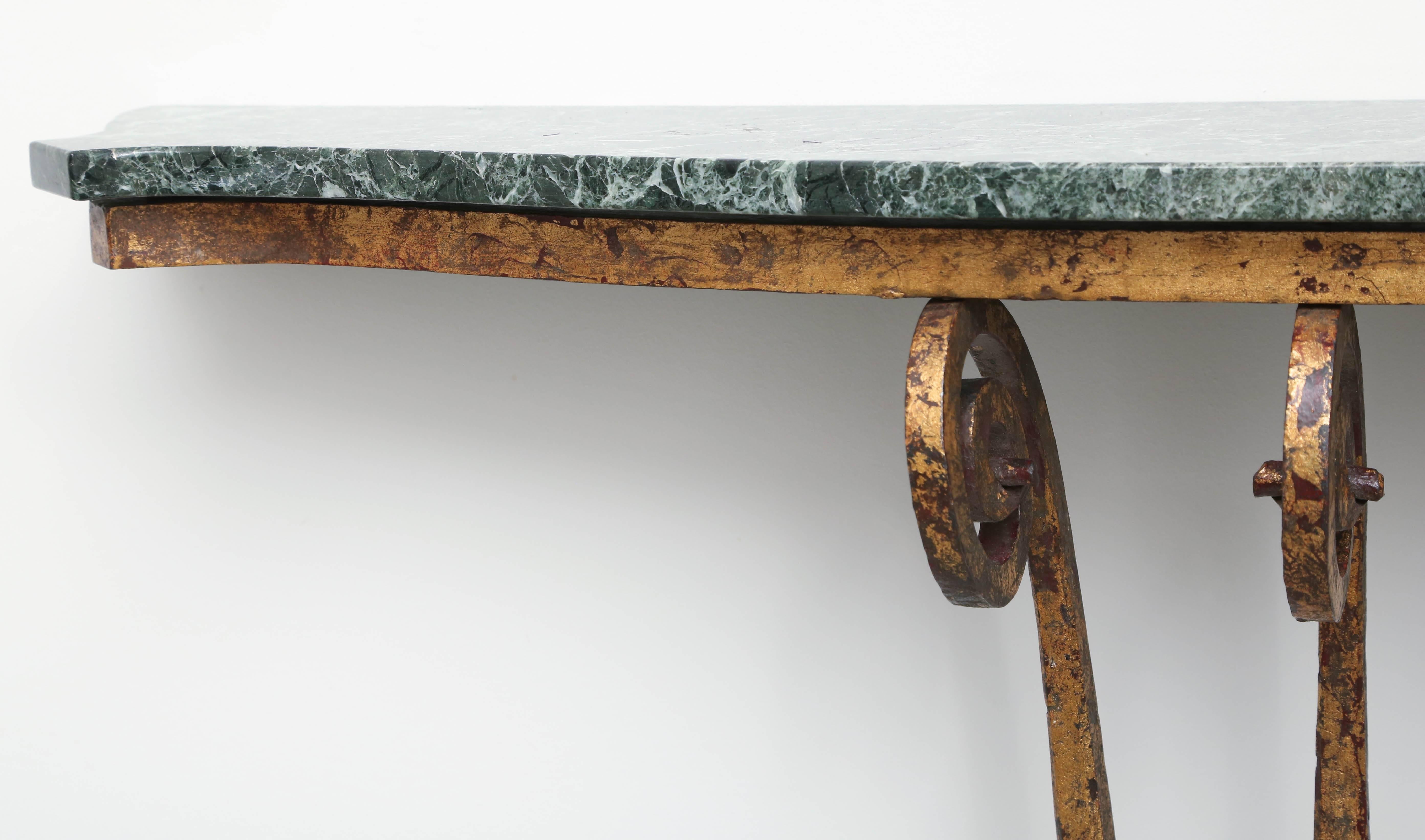 This handsome Art Deco wall-hung console is very much in the style of pieces created by Edgar Brand in France in the 1920s and 1930s. The piece is fabricated in wrought iron with a gilt-gold finish and a dark green variegated marble top. The central