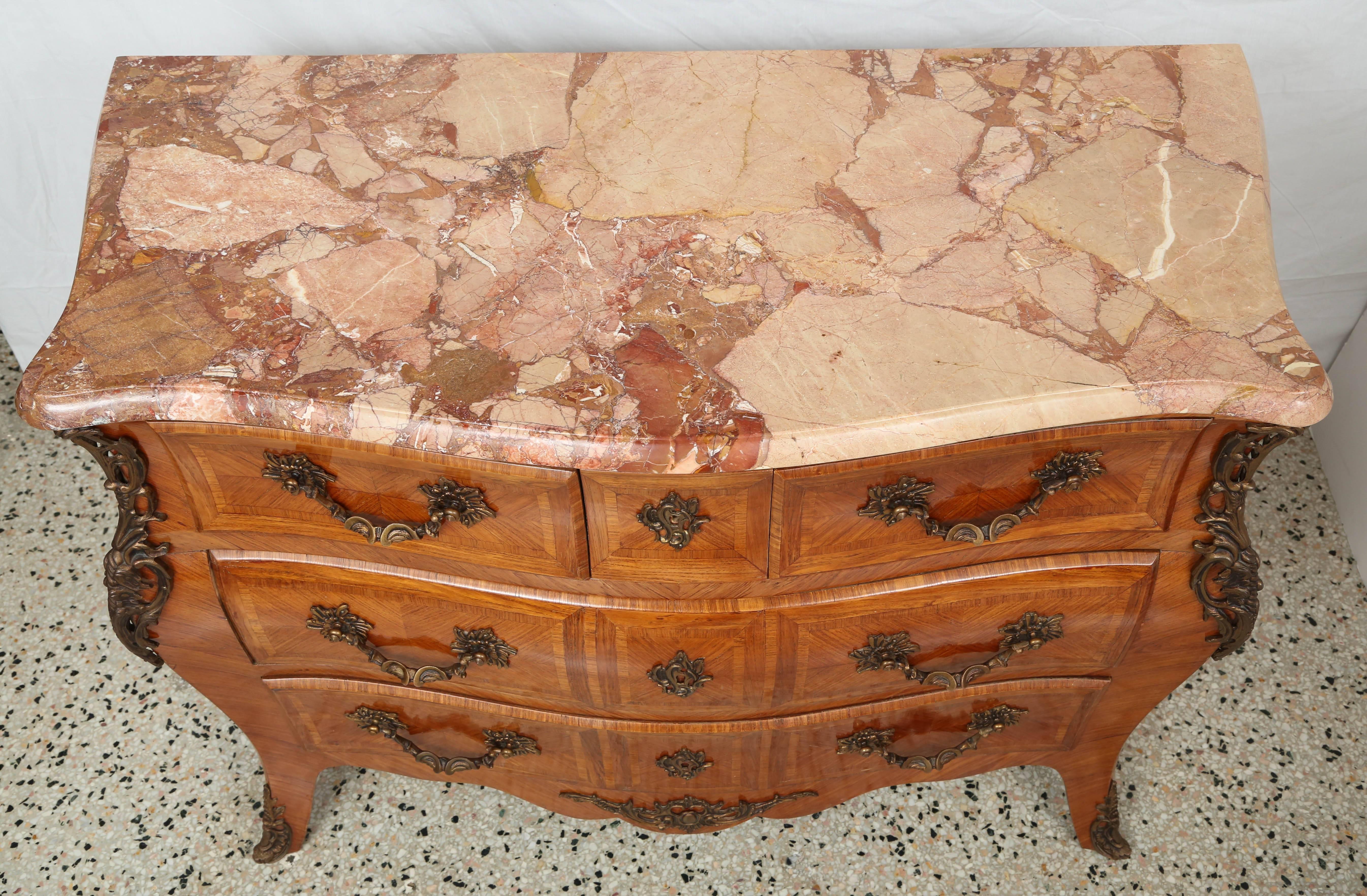 This beautiful Louis XV style commode was recently purchased in London and dates from the 1940s. The wood veneers are in a warm coloration which compliments the antiqued brass hardware. The marble top is variegated in colors of rose and