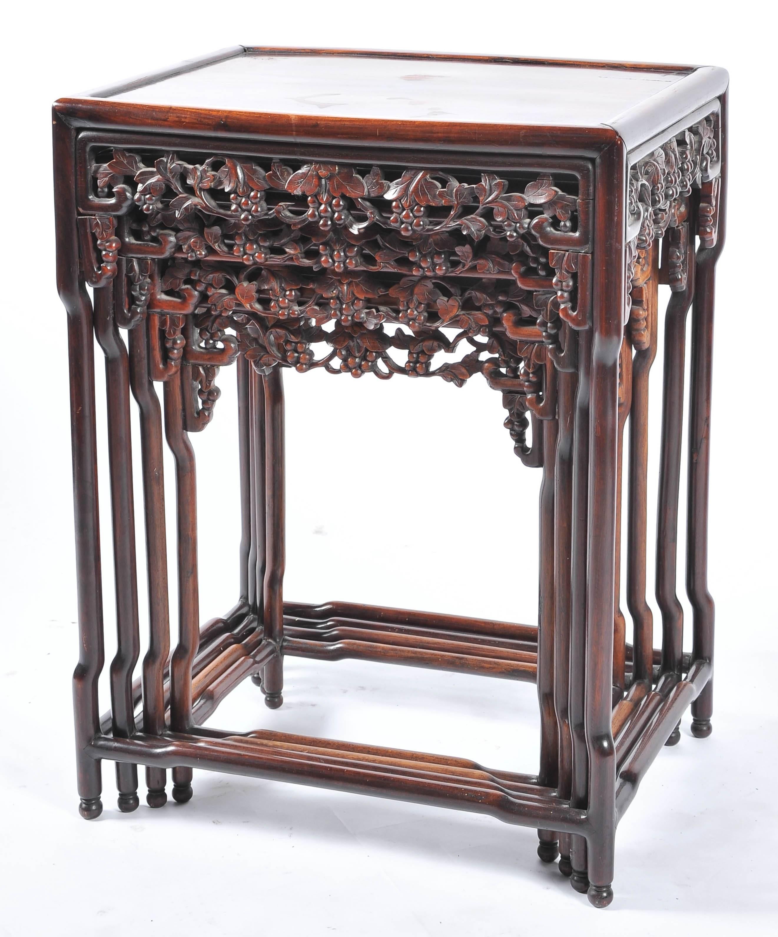 A good quality nest of four Chinese hardwood tables, each having carved and fret work frieze panels of leaves and grapes and raised on four turned legs, united by stretchers.