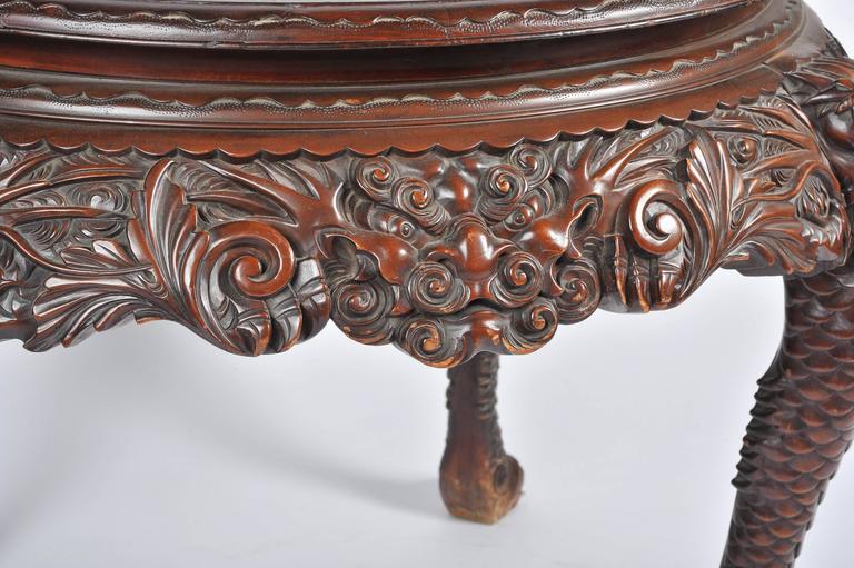 A late 19th century carved oriental centre table, having a polished top carved scrolls, leaf and mythical dragon masks to the apron. Raised on carved scale like cabriole legs that terminate in claw feet.