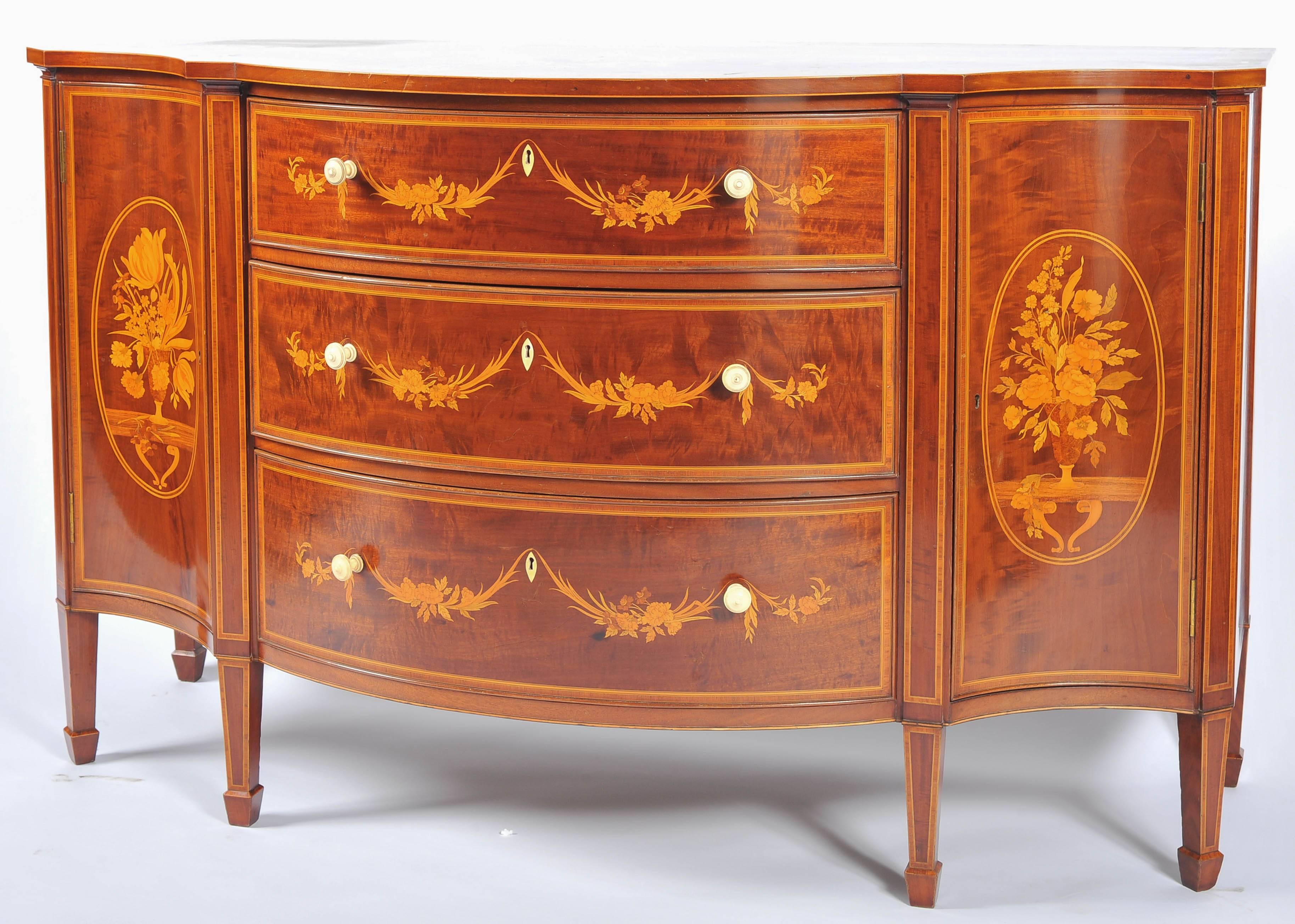 A very good quality Edwardian mahogany marquetry inlaid serpentine fronted side cabinet. Satinwood and boxwood inlaid marquetry panels, three graduating drawers to the centre, cupboard doors to either side and raised on square tapering legs with