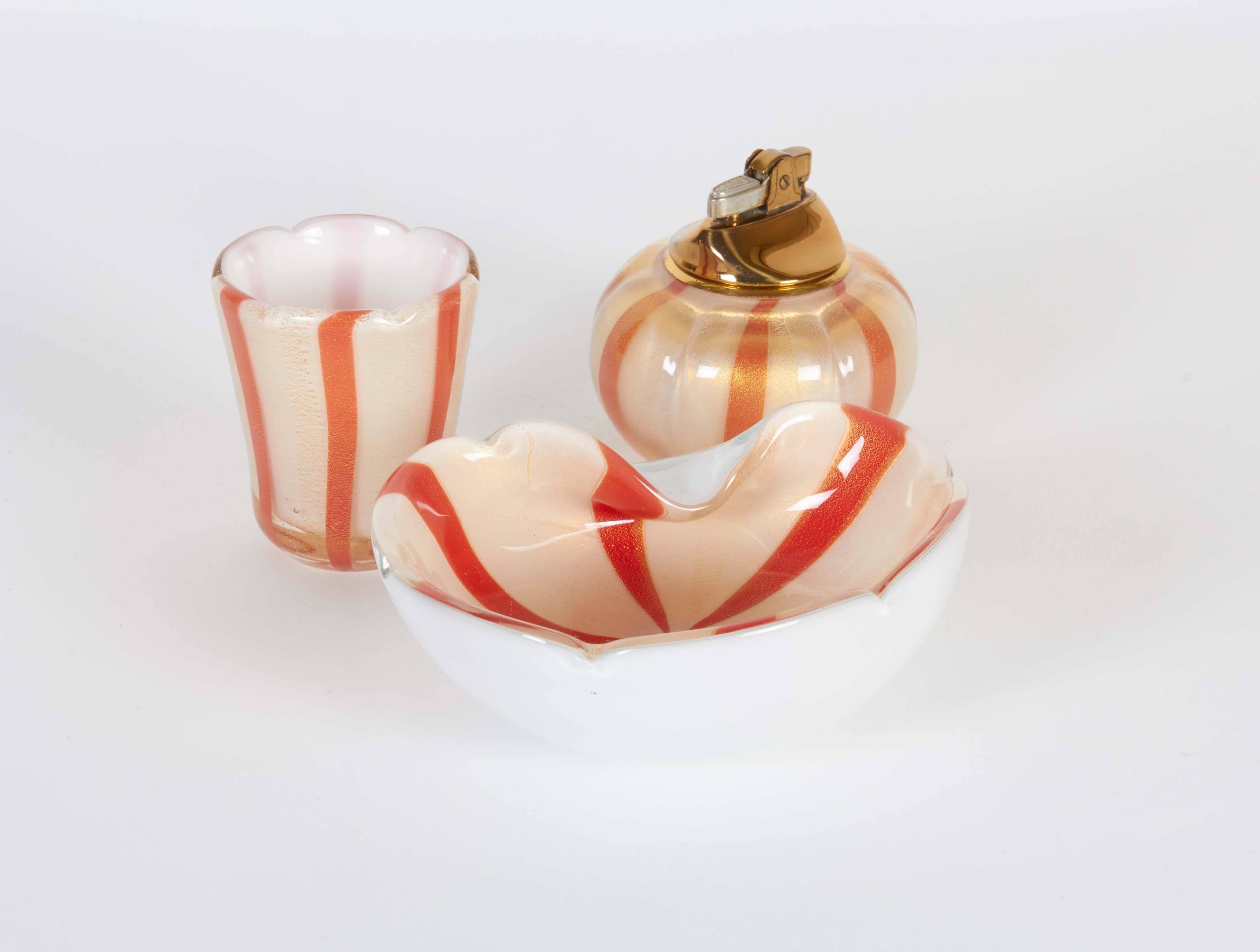 An Italian smoking set by Alfredo Barbini, including ashtray, lighter and cigarette holder in orange and white striped Murano glass, circa 1950s, detailed with gold flakes. Markings include stickers that read [Made in Italy] to the underside of the