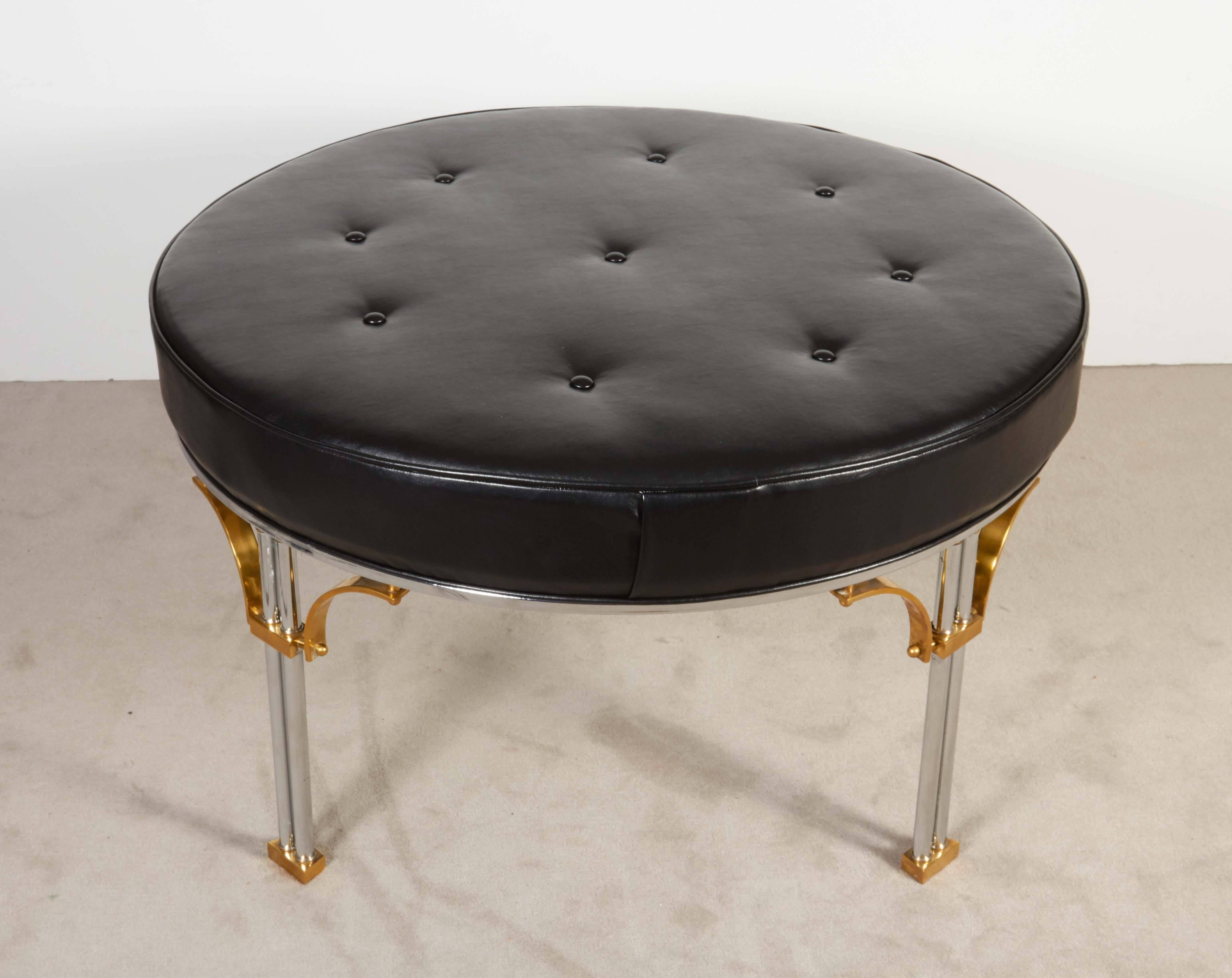 An ottoman by Maison Jansen, produced in France circa 1960s, with round seat in button tufted black faux leather, raised on four dual legs in chrome over steel, with brass accents. Very good vintage condition, consistent with age, newly