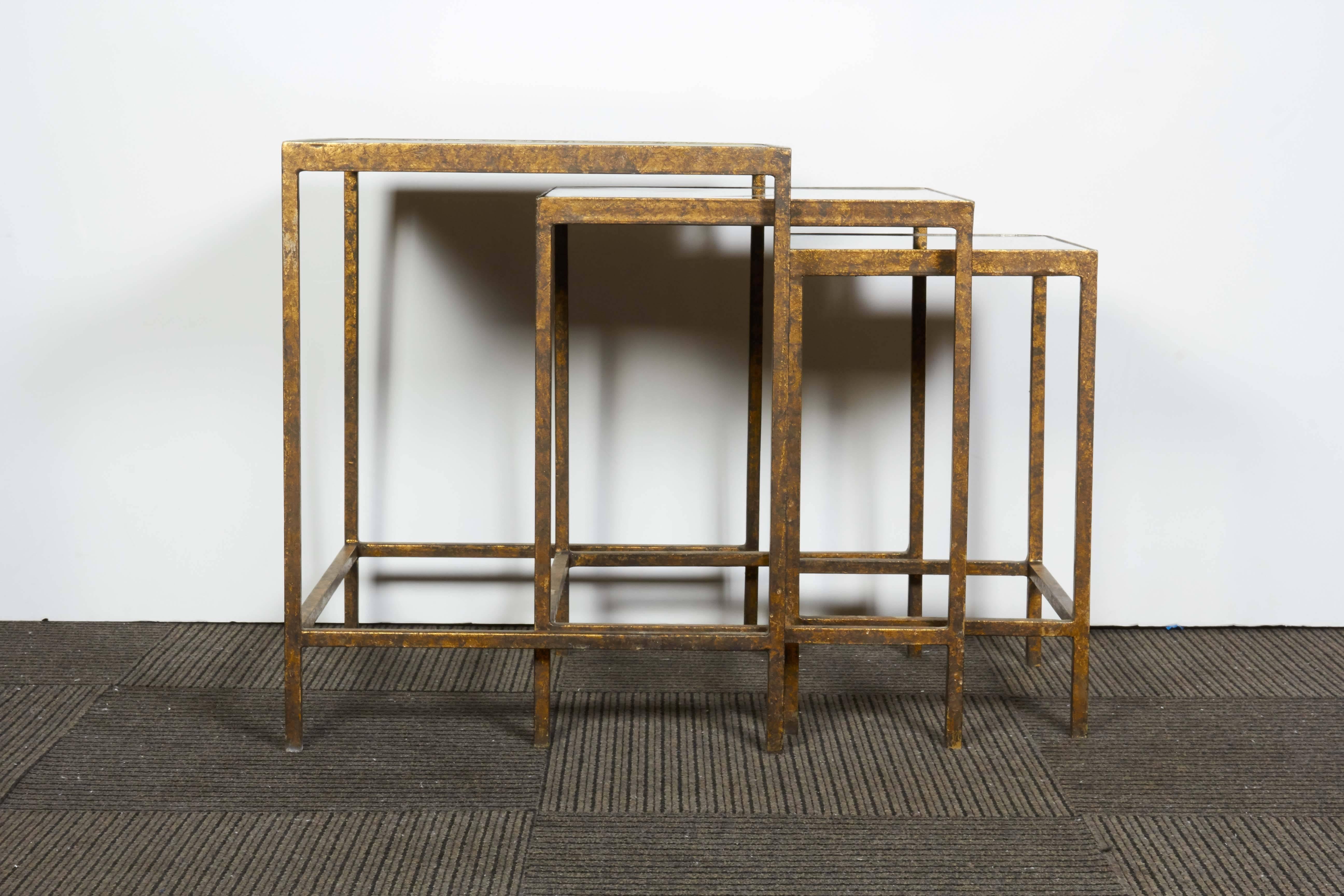 A contemporary set of three antiqued nesting tables with beveled mirror tops set against gilt metal frames. The tables remain in very good condition, wear consistent with prior use.