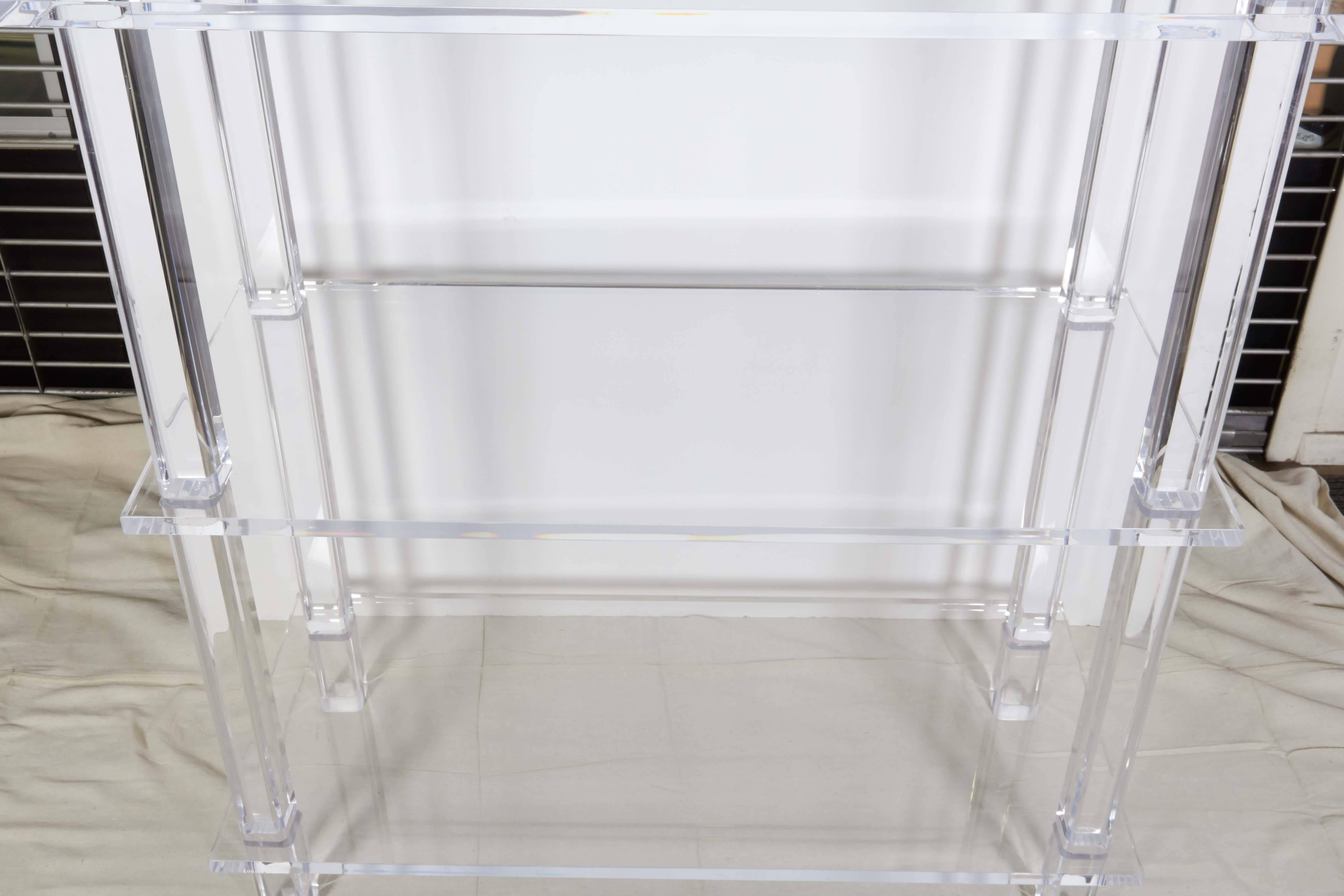 A tall modernist style etagere entirely in clear Lucite, shelves raised on thick beveled legs. Excellent condition, minuscule wear, consistent with age and use.