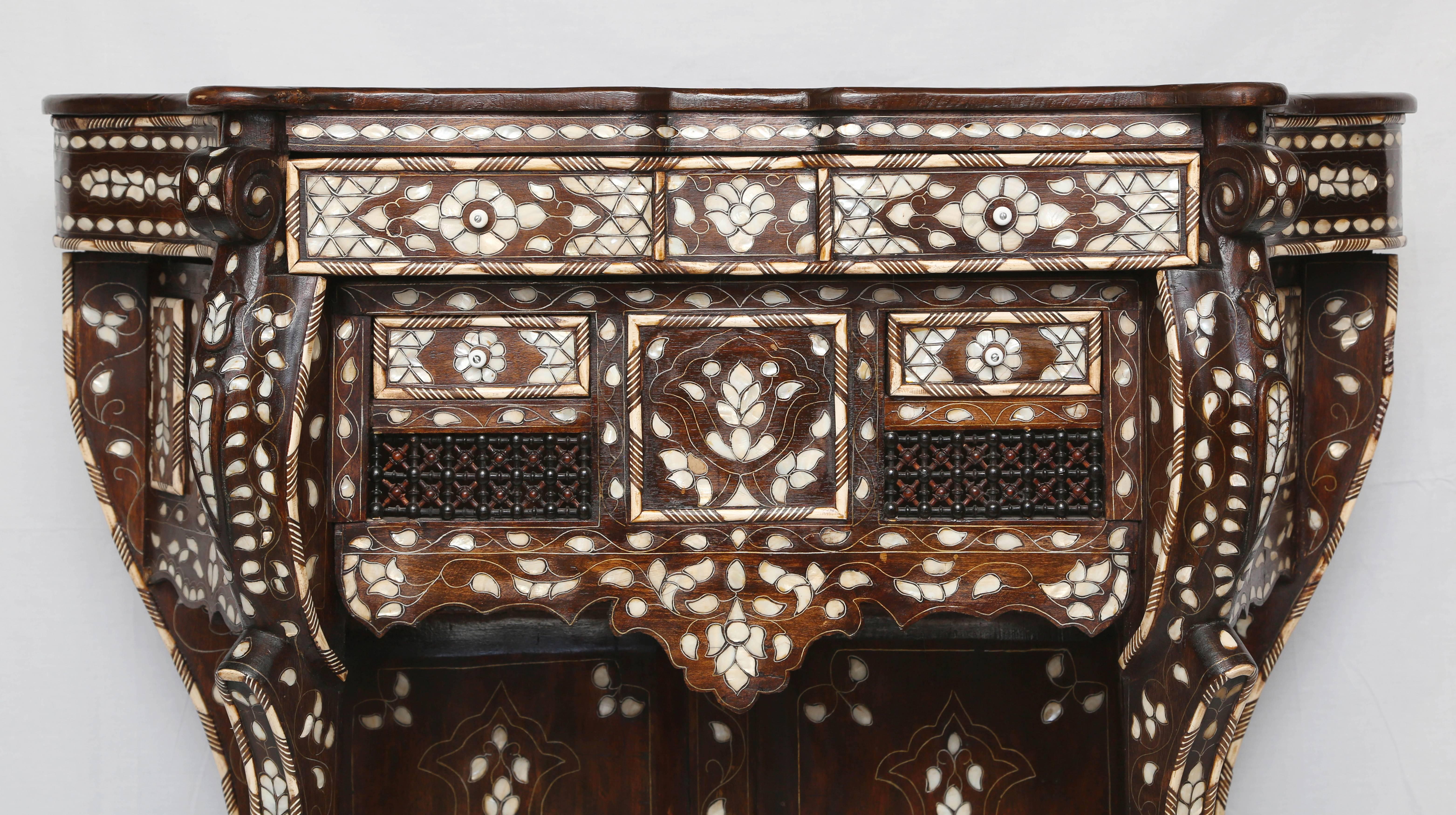 Superb Syrian mother-of-pearl inlaid console, the shaped top inlaid with floral tendrils, surmounting the conforming case having one over two drawers with ball and spindle detailing and shaped pendant apron rising on C-scroll legs conjoined by a