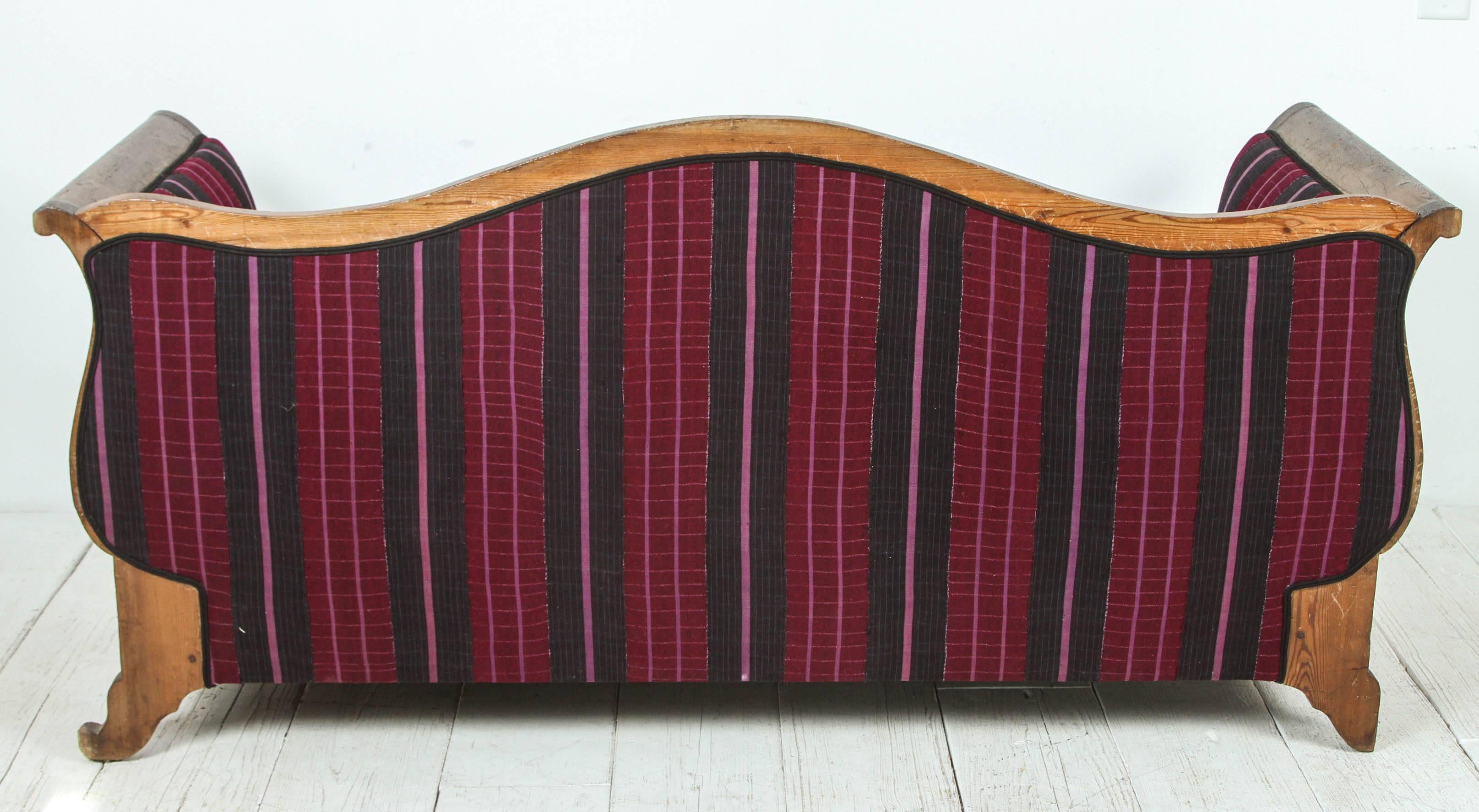 Upholstered curved settee with pink and black stripe fabric.