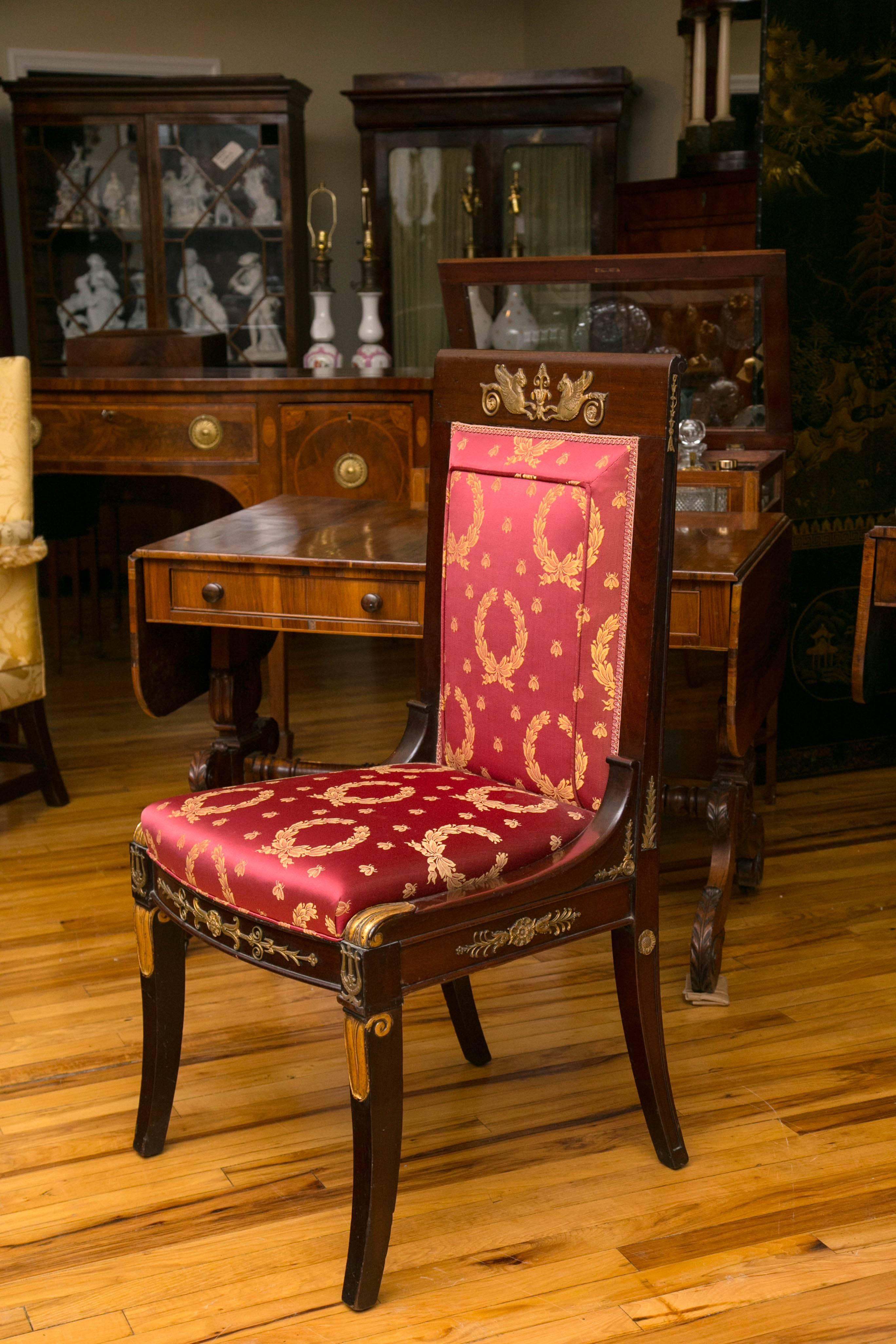 A mahogany upholstered high back chair with finely cast ormolu mounts. The crest rail is adorned with a pair of Empire style ormolu griffin. The front and side rails are mounted with foliate design, while the saber legs feature lyre mounts and gilt