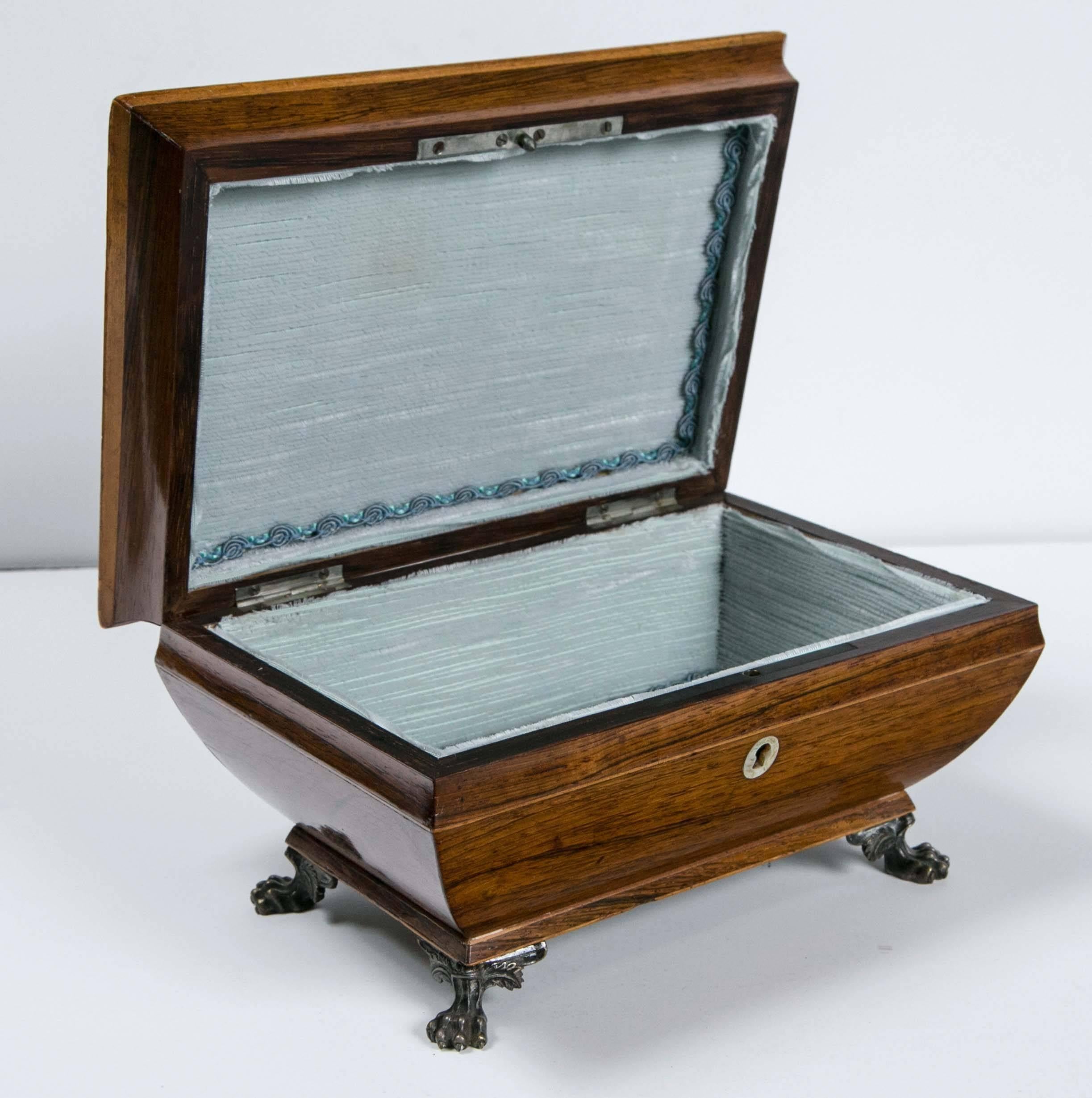 Antique 1820 rosewood jewelry box. It has mother-of-pearl inlay, brass feet, and an unusual shape. The box with its petite small feet, gives it a tier layer illusion. The inside is light blue satin with a deeper blue brocade welting. It has no key.