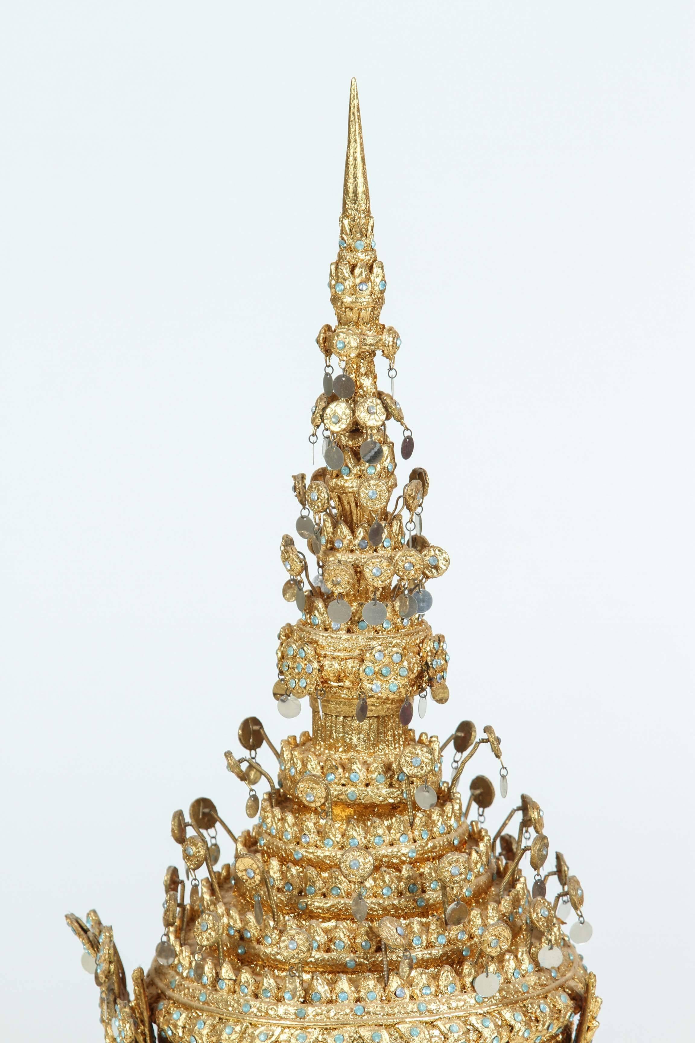 Ceremonial Thai headdress usually worn for wedding or religious ceremonies.
Gilt ceremonial headdress circa 20th century, hand-crafted in Thailand.
A traditionally modeled design with a conical metal spire at the top, in gilt papier mâché, metal