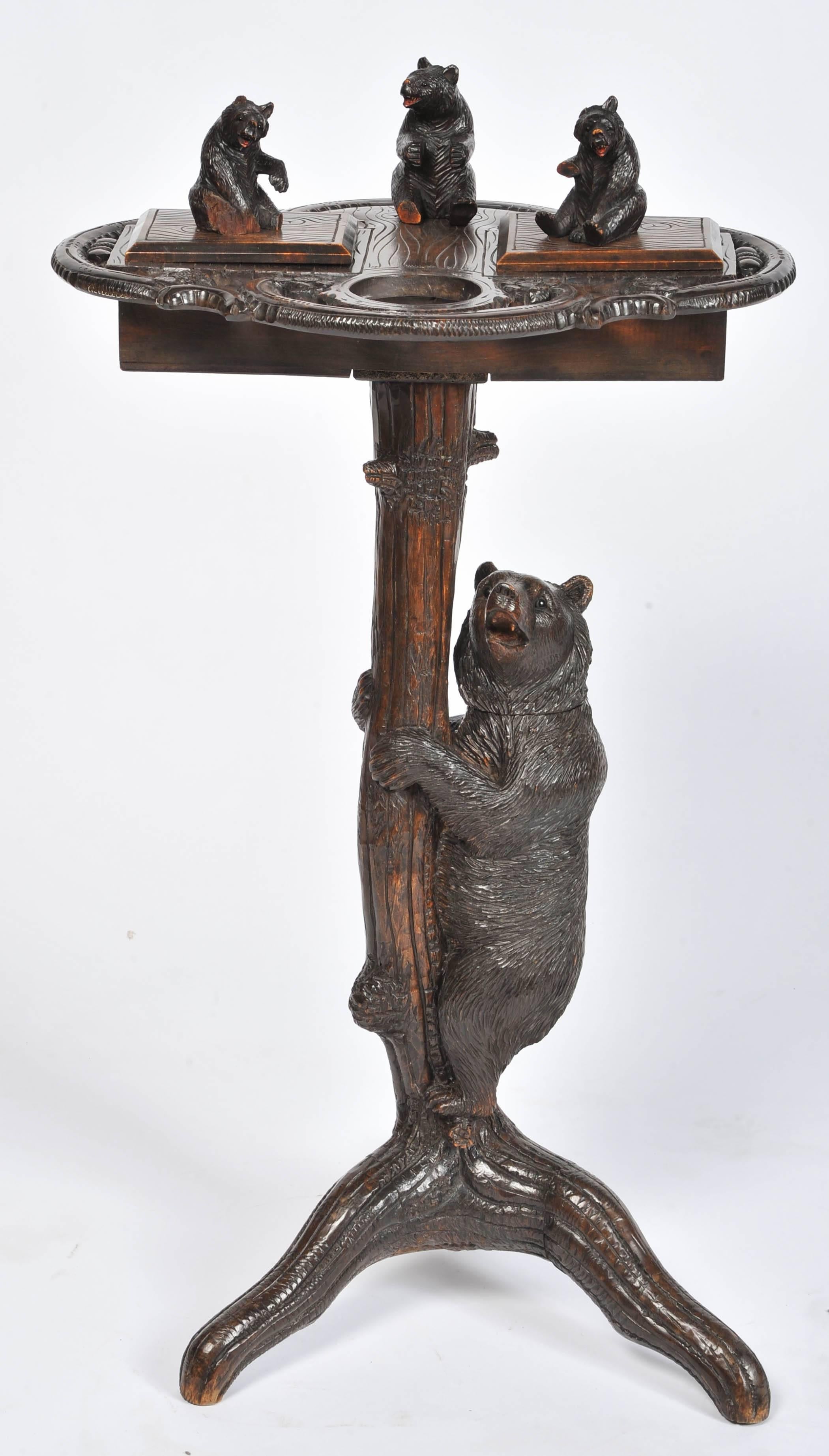 A 19th century carved black forest smokers stand, having three carved bears on the top, two lidded compartments. Supported by a large bear climbing a tree. A brass dish fits in the circular cut-out.