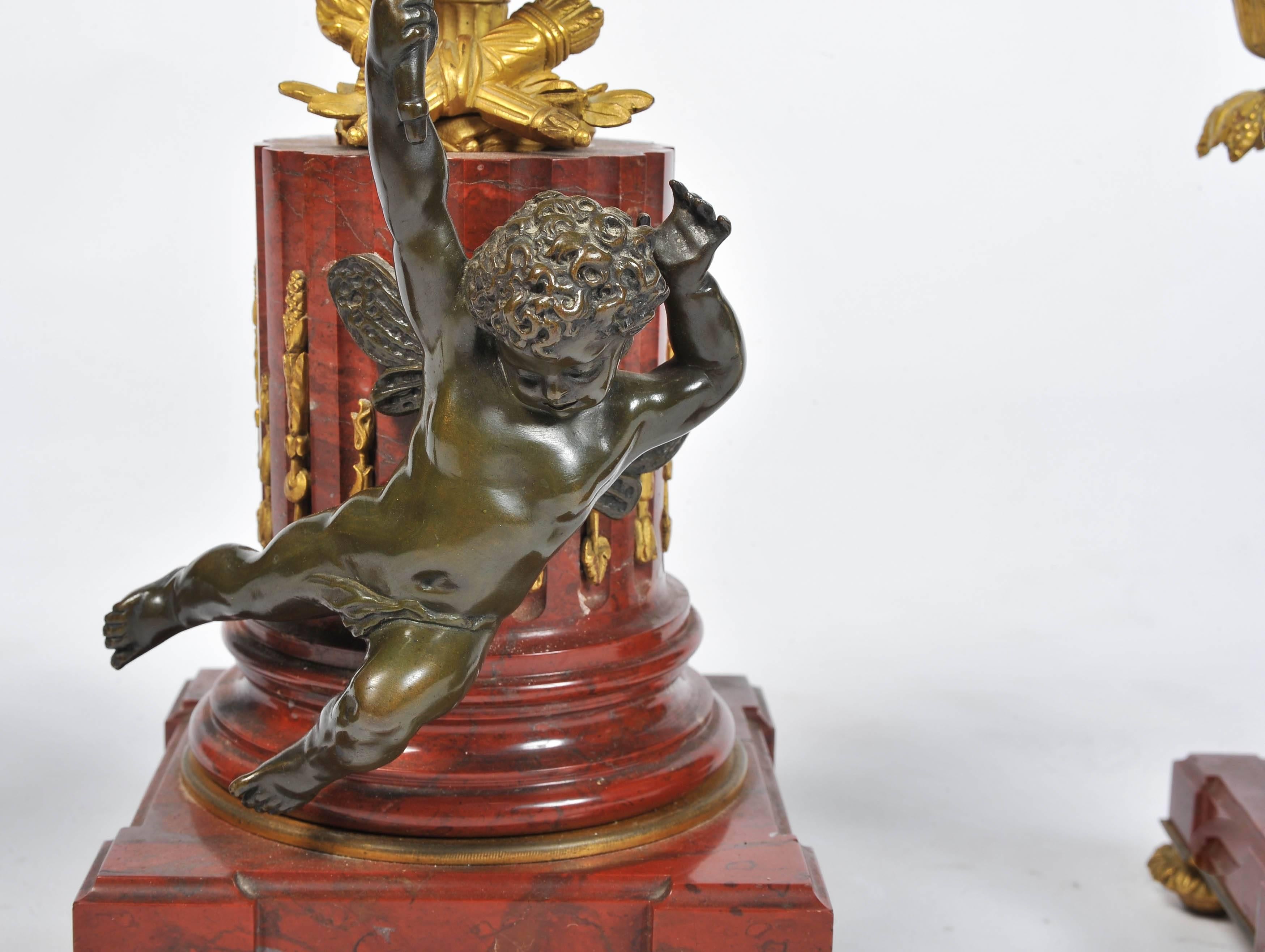 A good quality French gilded ormolu, bronze and Rouge marble ball clock garniture. Having a gilded cherub to the top, a bronze cherub mounted on the rouge marble pedestal base. A pair of five branch gilded ormolu candelabra on rouge marble bases.