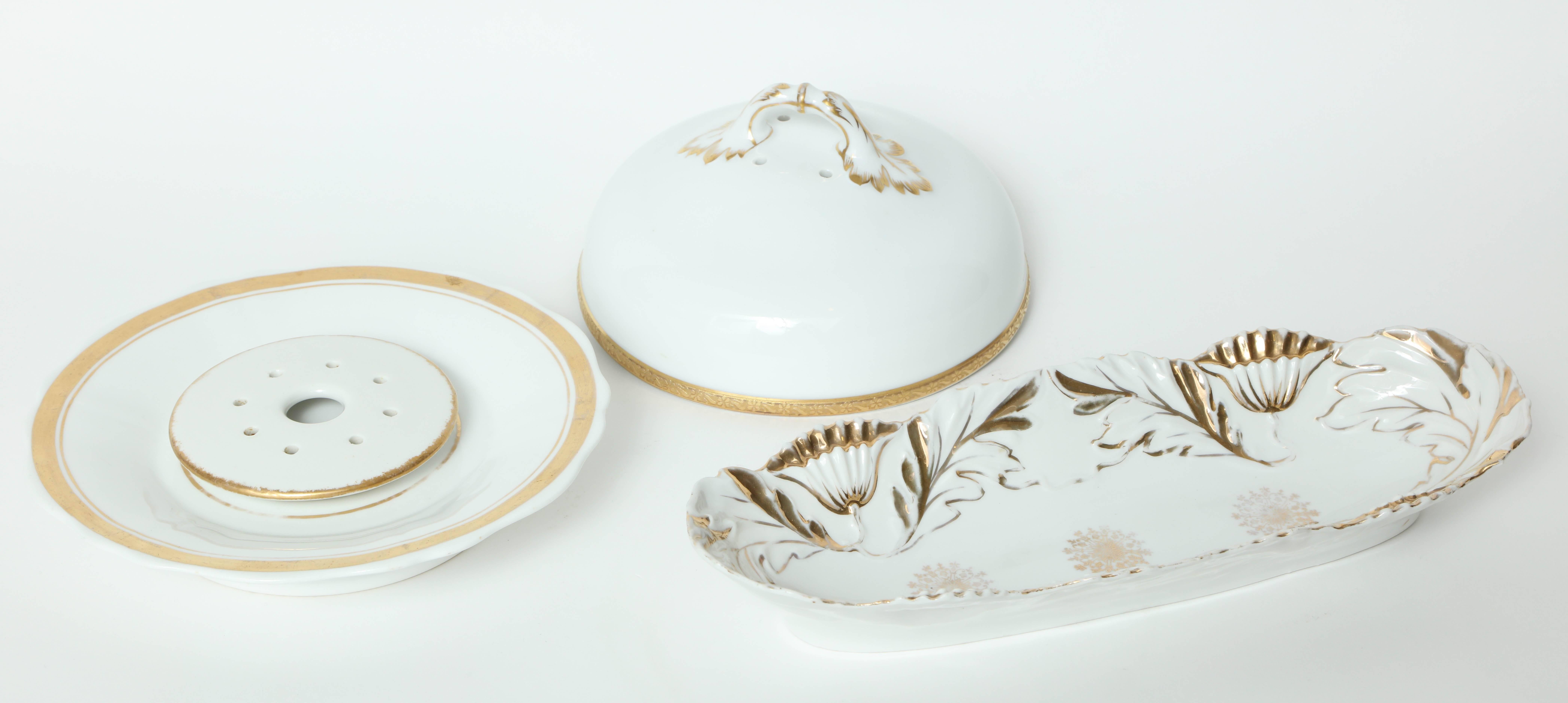Set of two French 1940s porcelain serving pieces with gilt accents. Set includes a covered butter/cheese server with stylized leaf handle and an oblong serving vessel with stylized floral border in the interior.

Oblong vessel measures 11 7/8