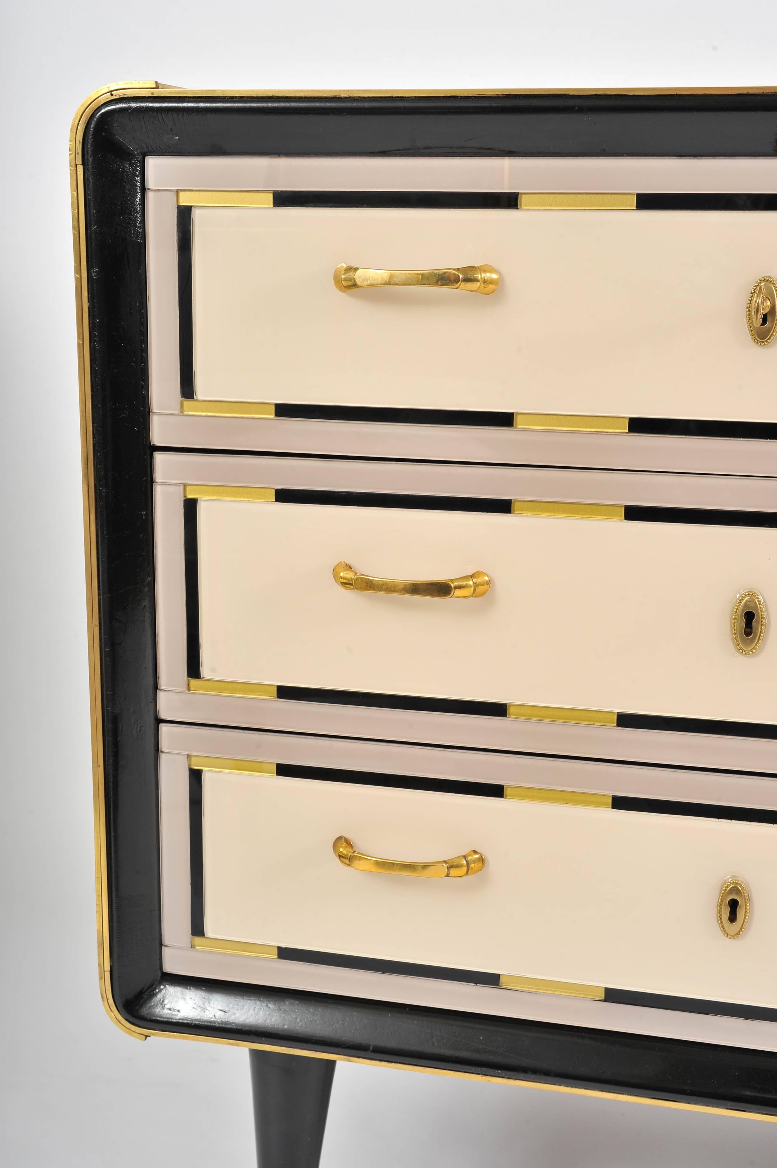 Subtle combination of cream glass drawers all with dusty pink surround and black and gold details. Black glass top with curved corners. Brass handles and sabots on turned wooden legs.